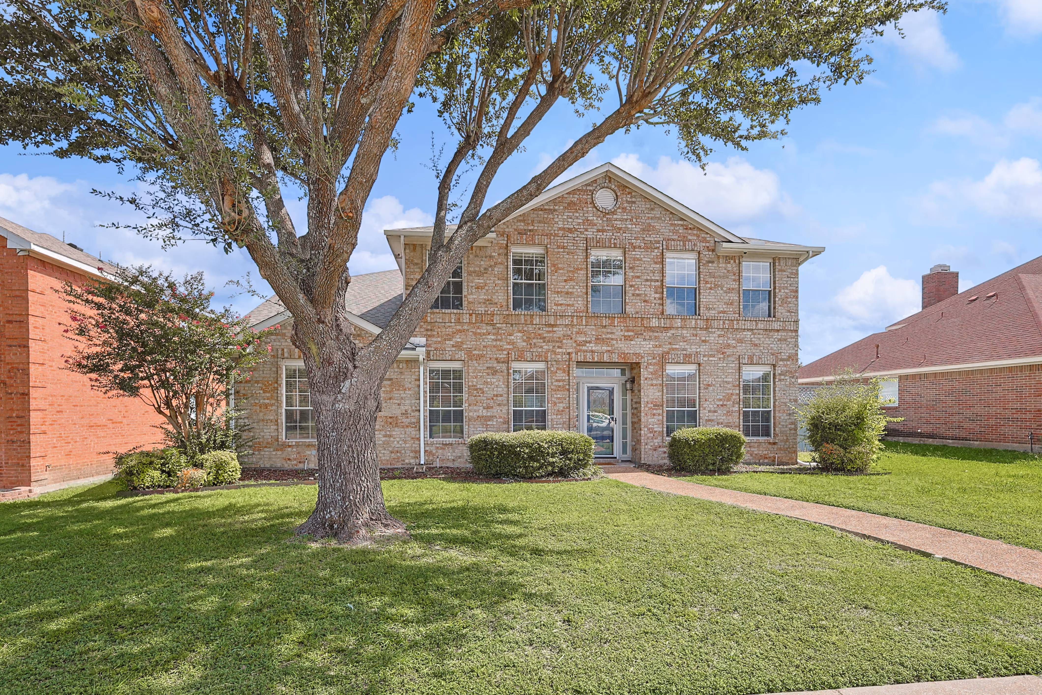 Front facade — two-story brick home framed by a large shade tree.