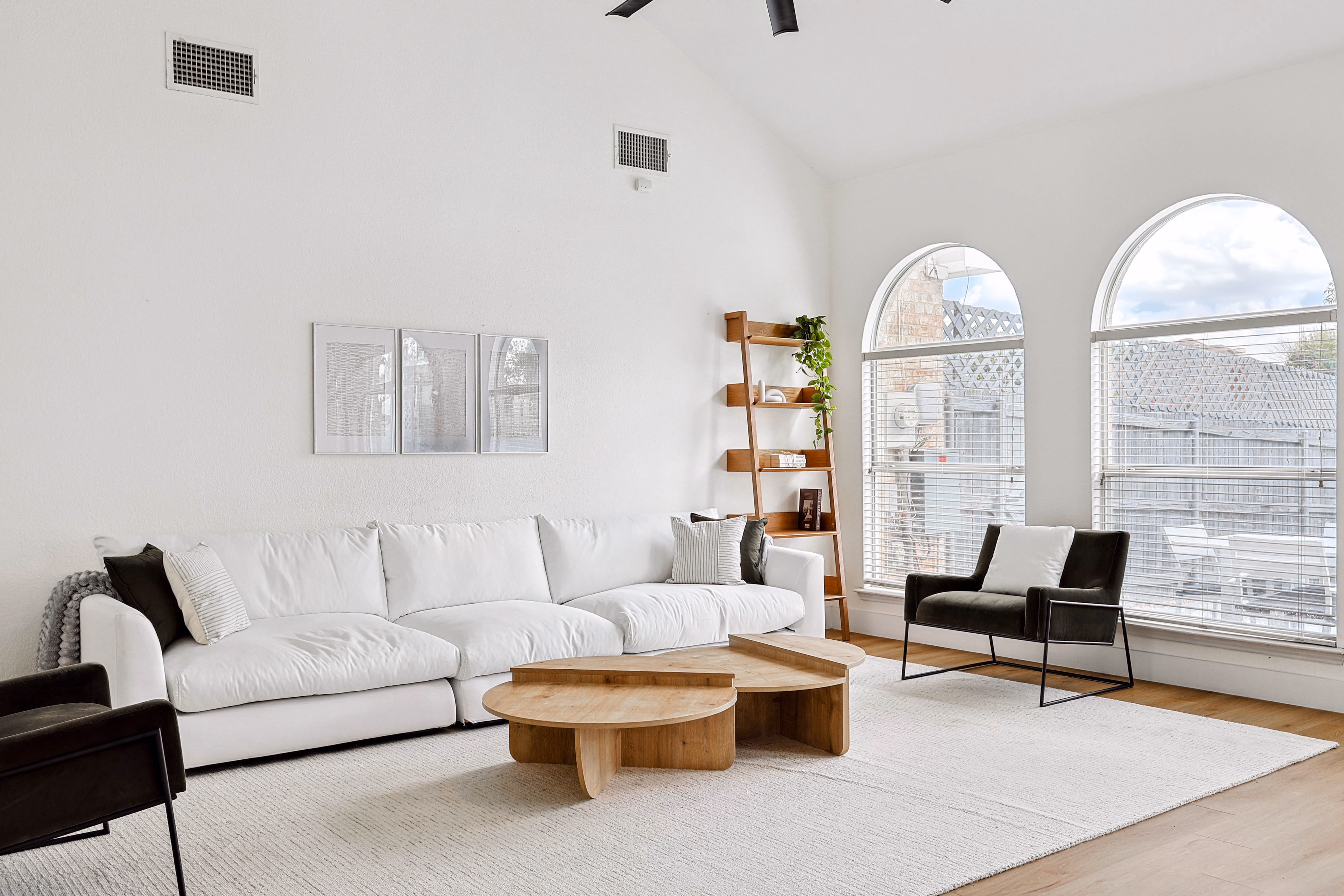 Great room — sectional and accent chair under oversized industrial ceiling fan, two-story arched windows.