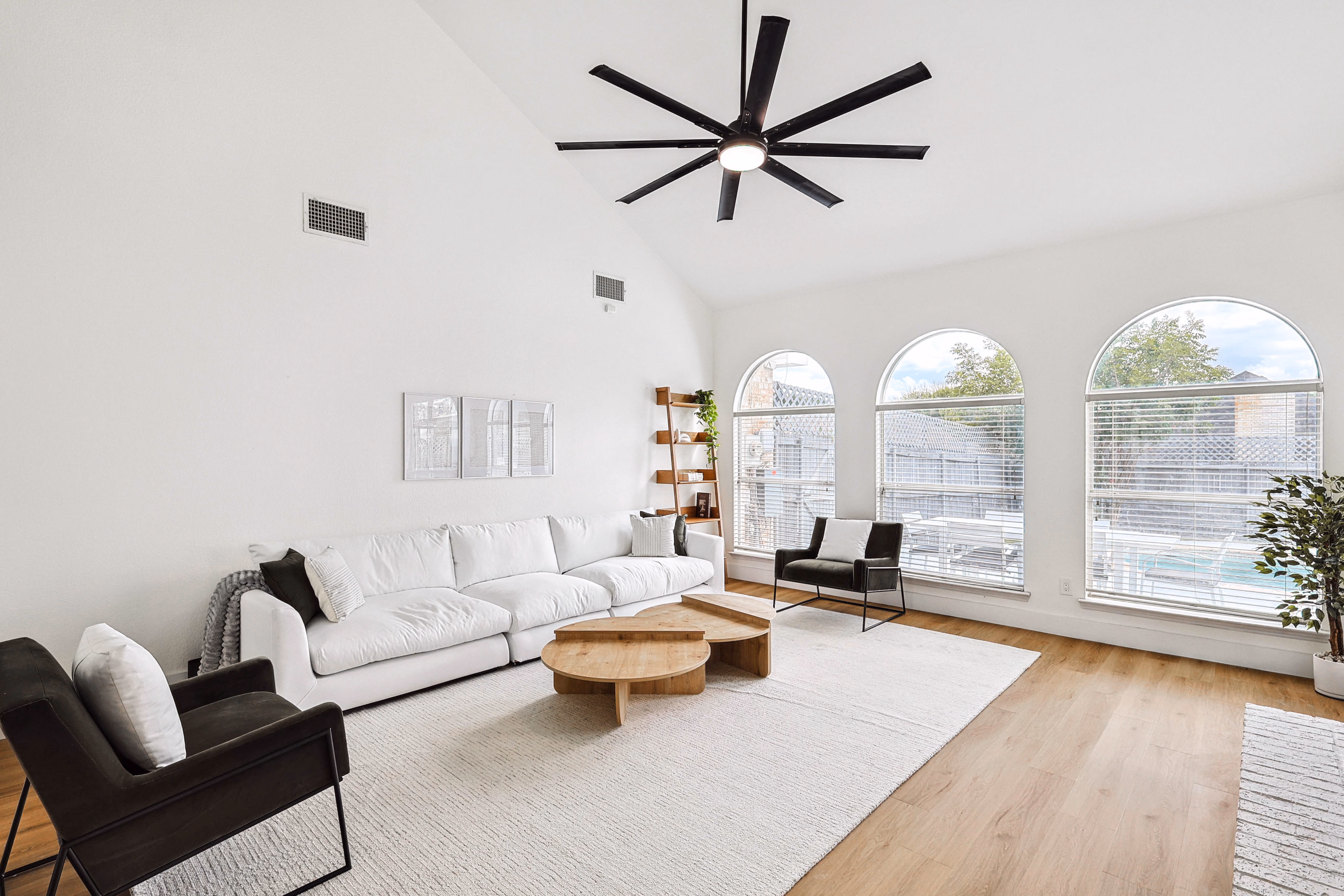 Great room from foyer — staircase to loft, sectional, oversized fan and abstract art trio.