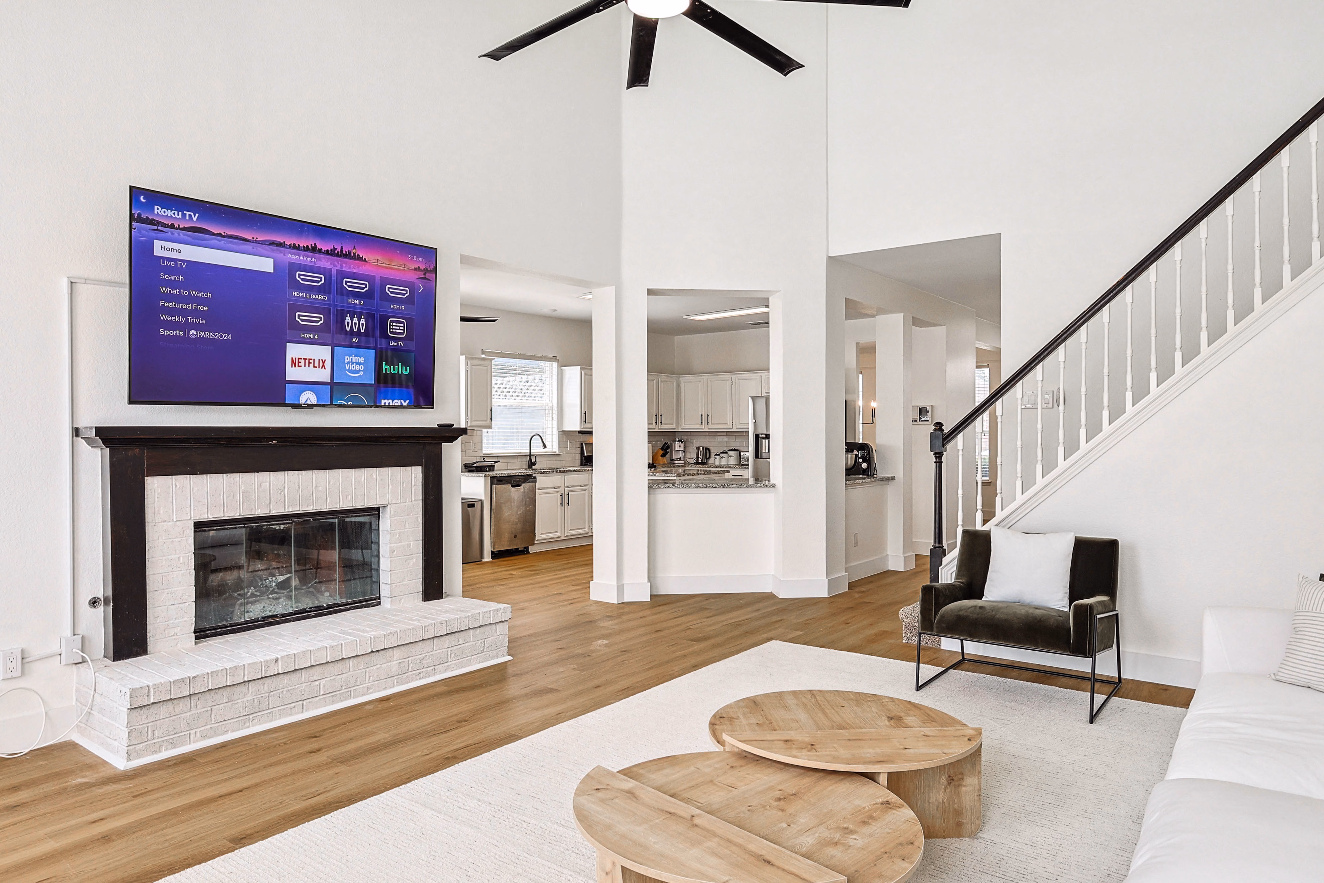 Great room — fireplace and TV centered on brick mantel, view into kitchen and breakfast nook.