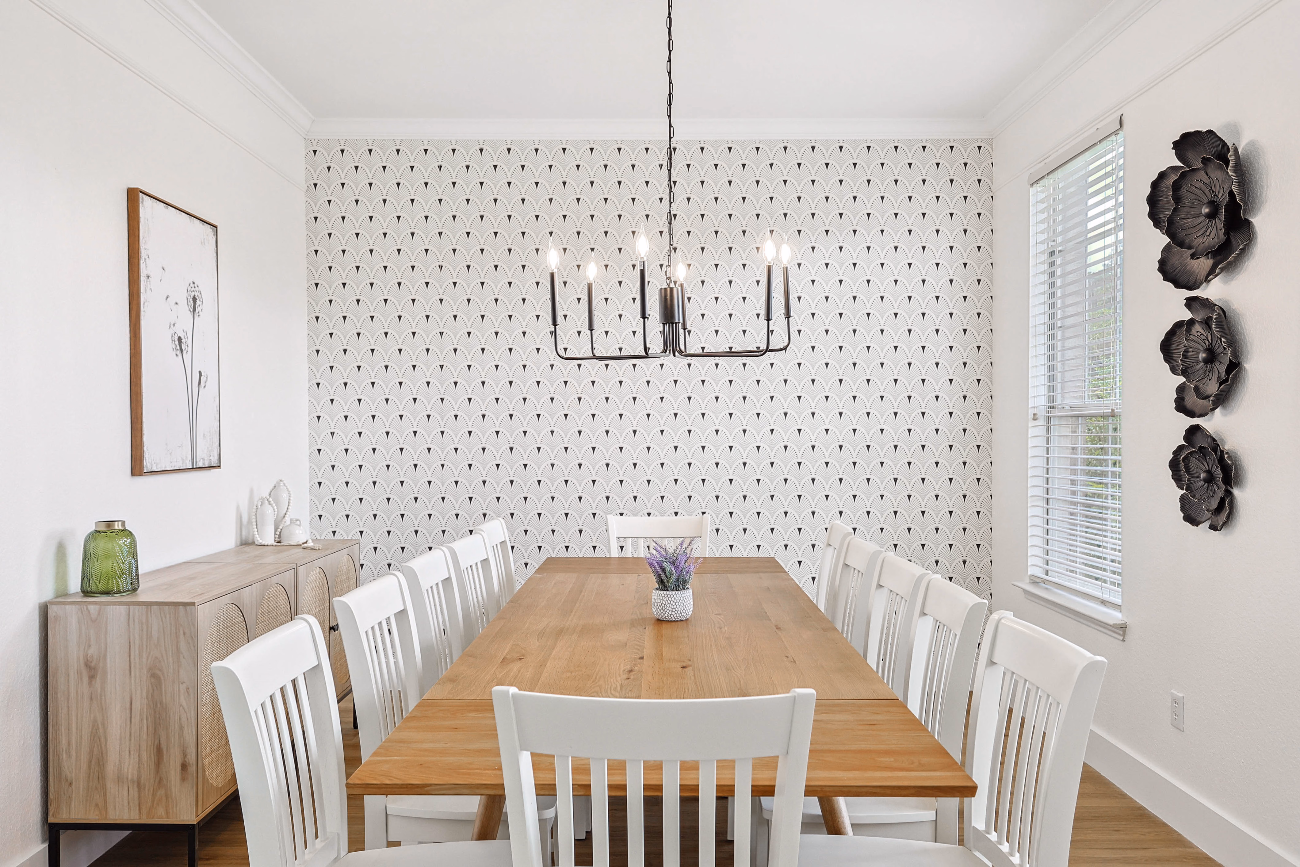 Dining room from the table — chandelier, accent wall, oversized window with metal floral wall art.