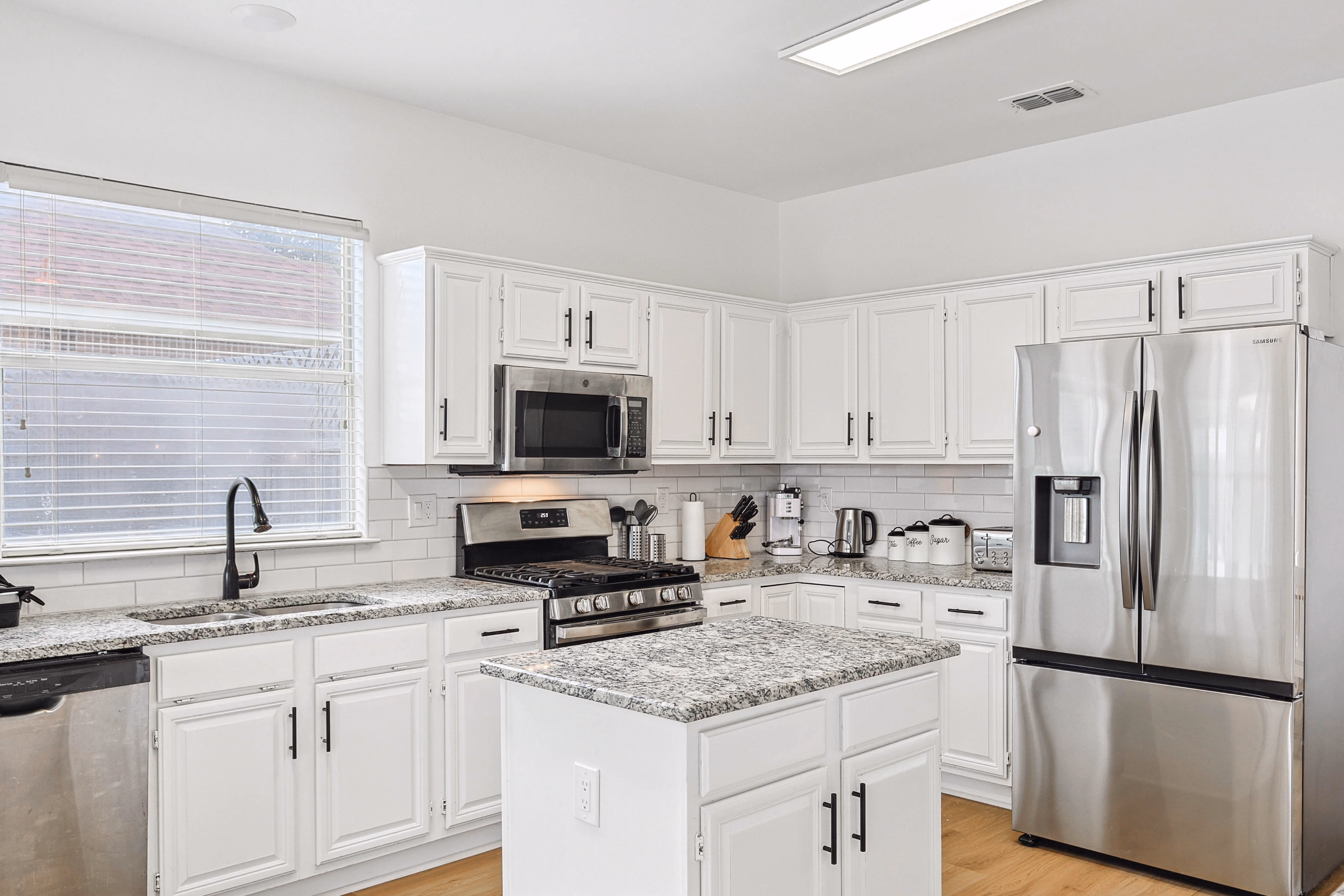 Kitchen — corner detail with knife block, kettle, toaster and labeled coffee/tea/sugar canisters on subway-tile backsplash.