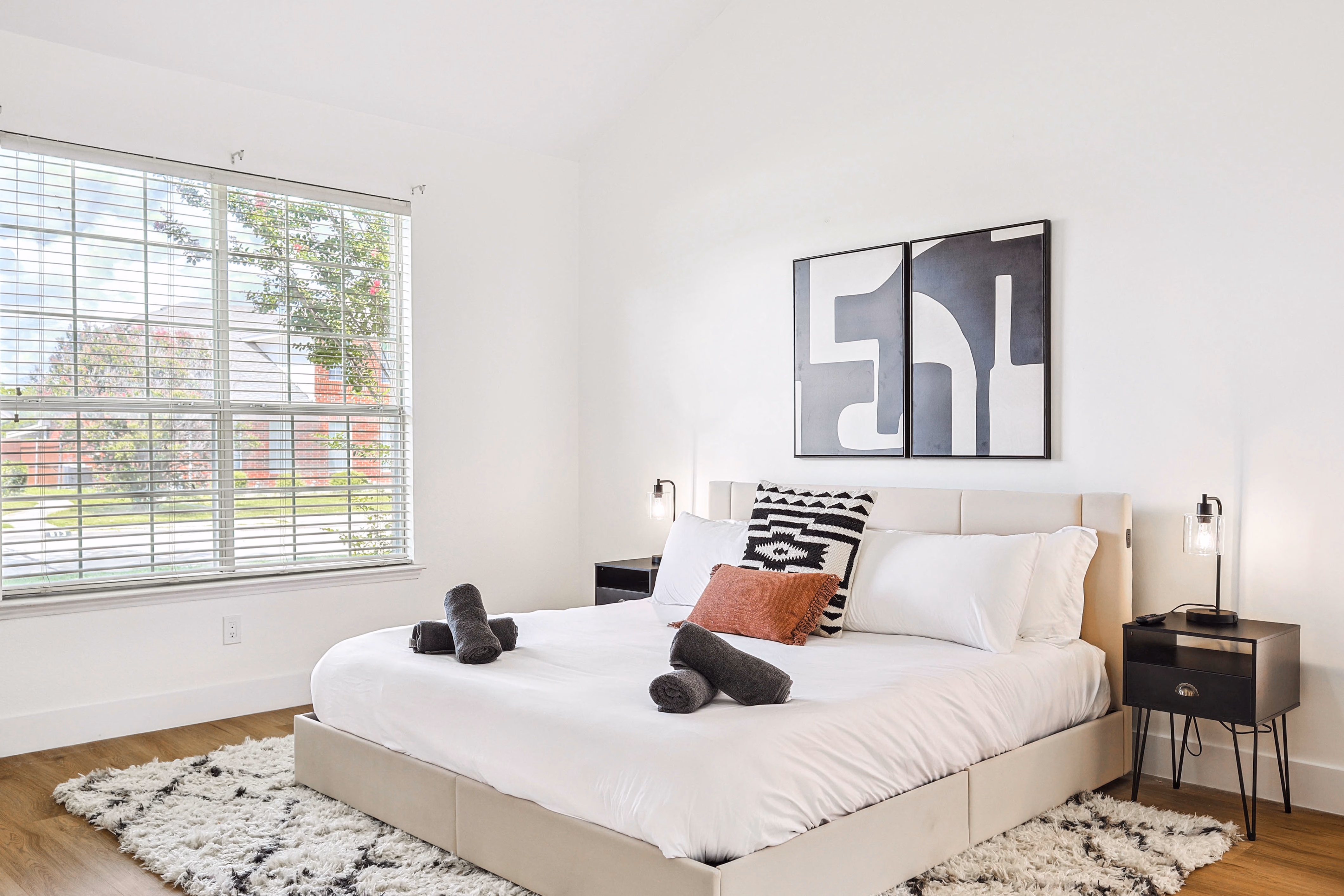Primary bedroom — close-up of bed with abstract diptych and matching nightstand lamps.