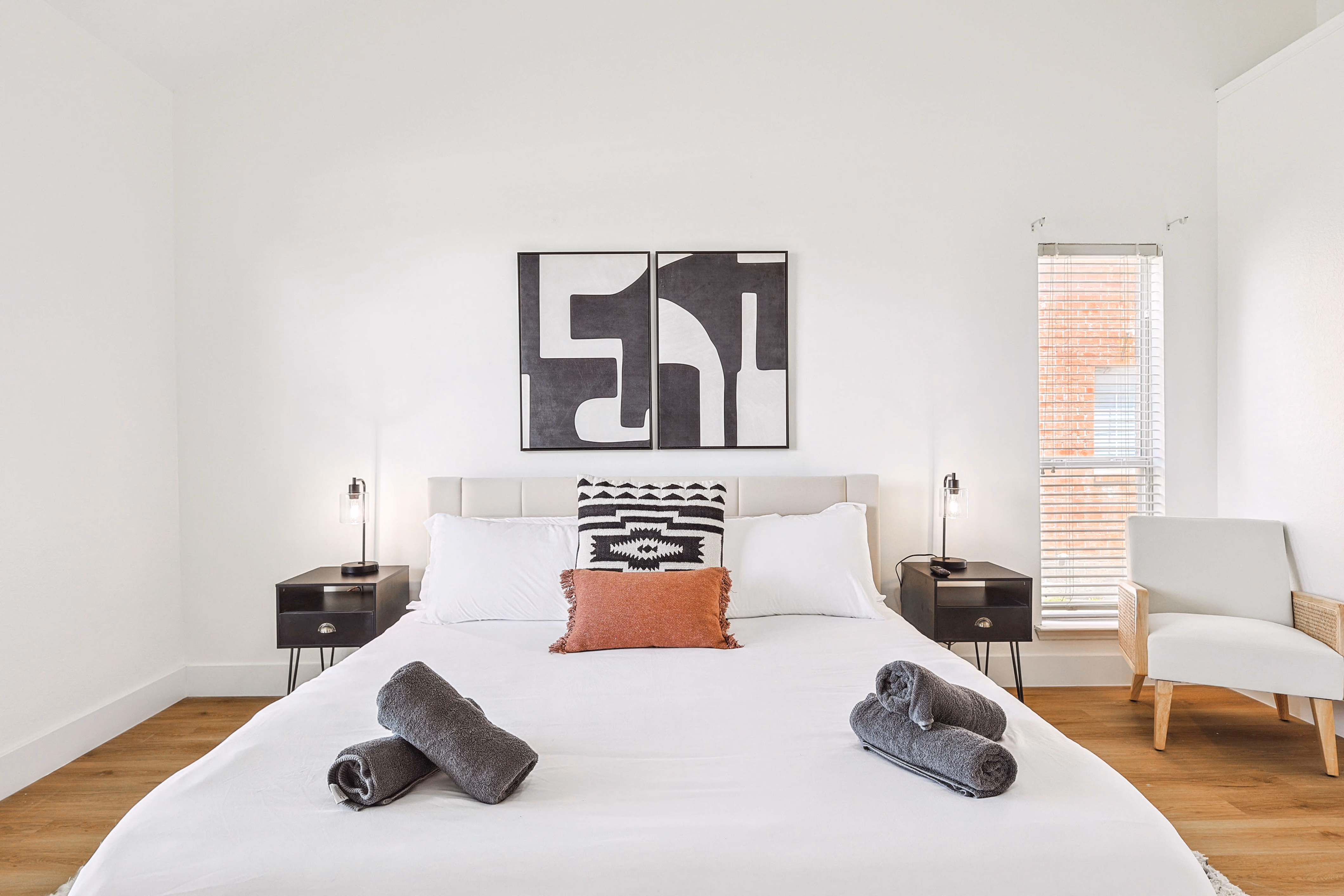 Primary bedroom — straight-on of the king bed and abstract artwork, nightstand lamps lit.
