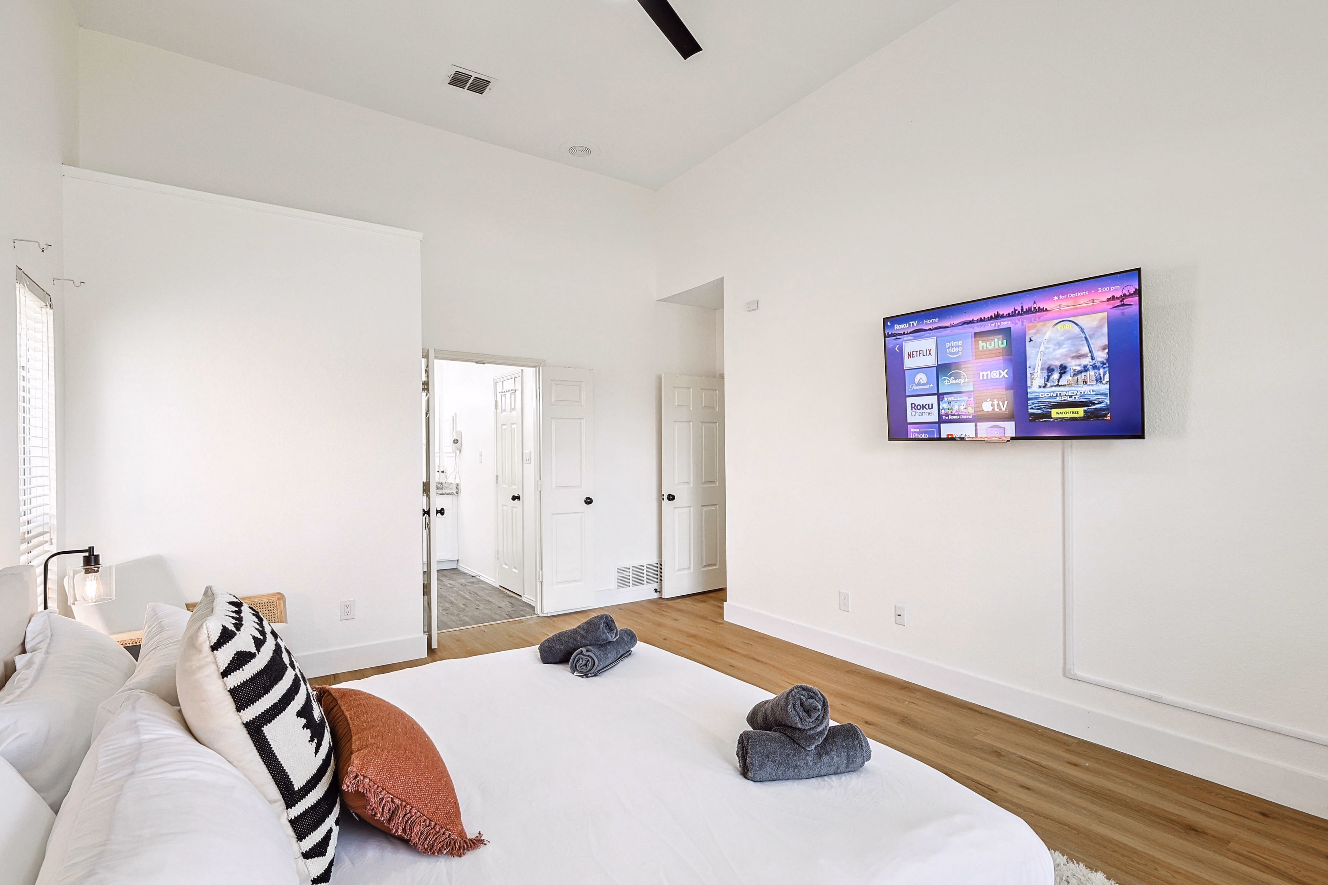 Primary bedroom — wall-mounted TV opposite bed, en-suite bath doorway visible.