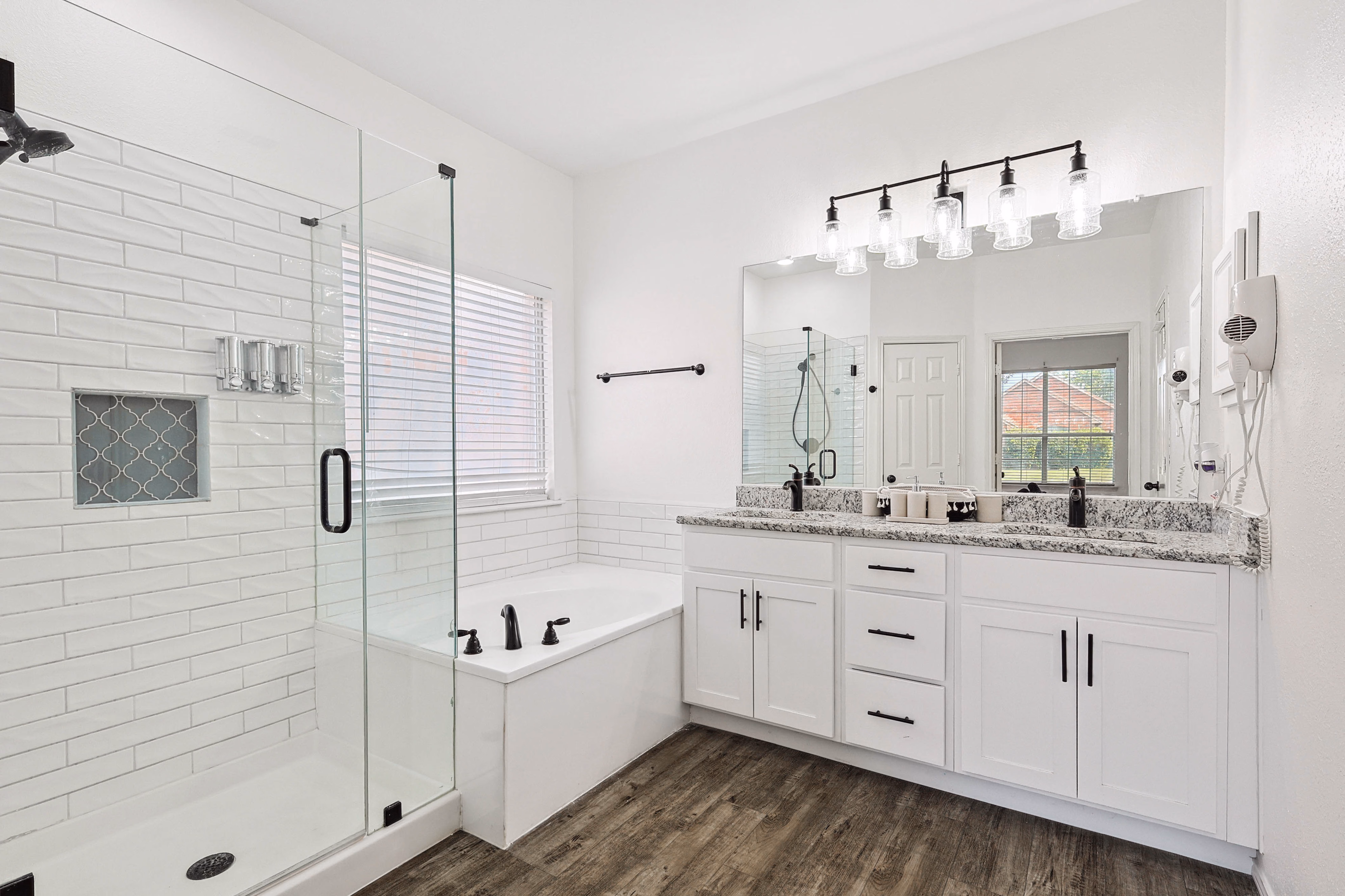 Primary bath — glass walk-in shower with subway tile, corner soaking tub, double granite vanity, five-bulb vanity light.