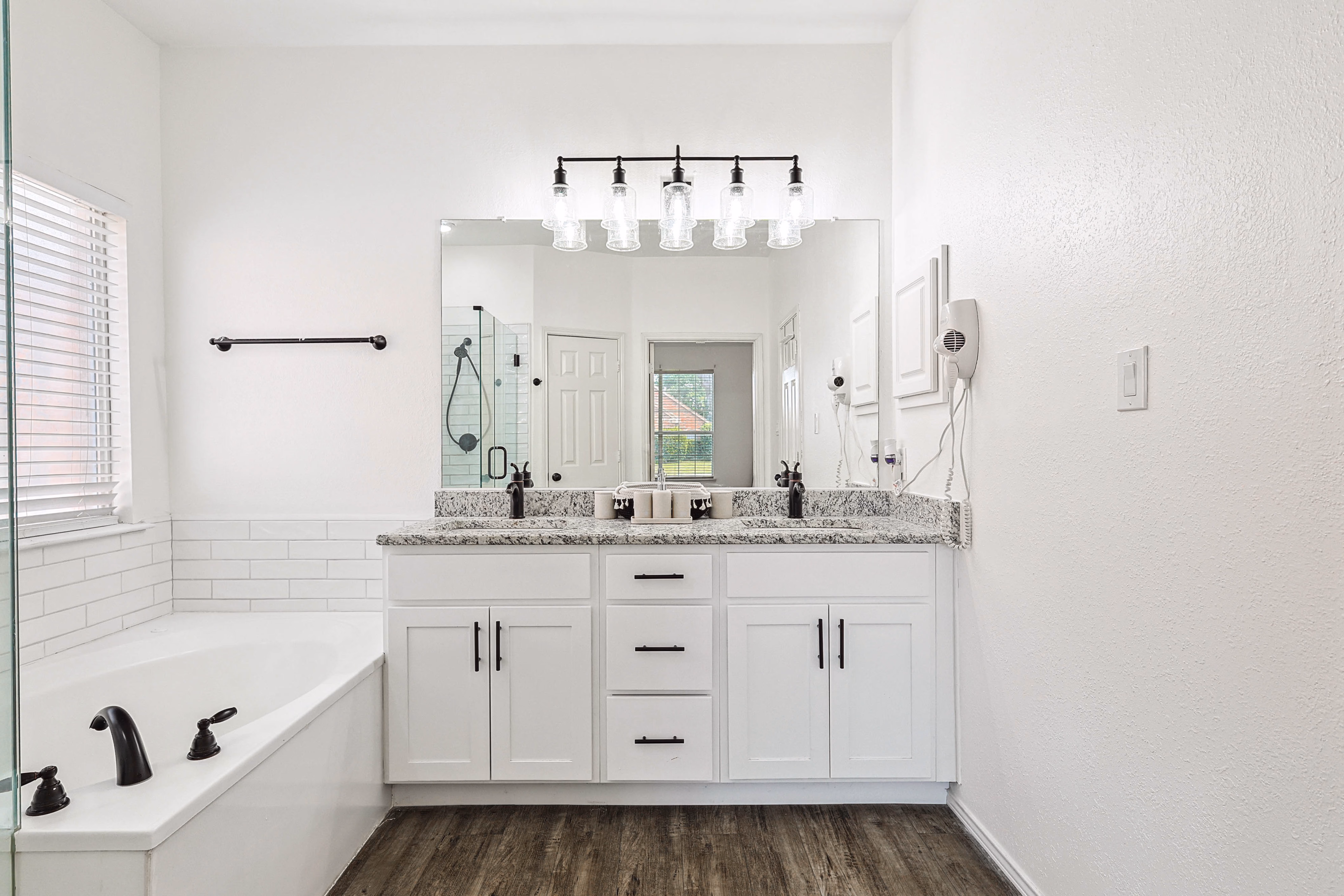 Primary bath — double granite vanity with bronze fixtures and large mirror, soaking tub on the left.