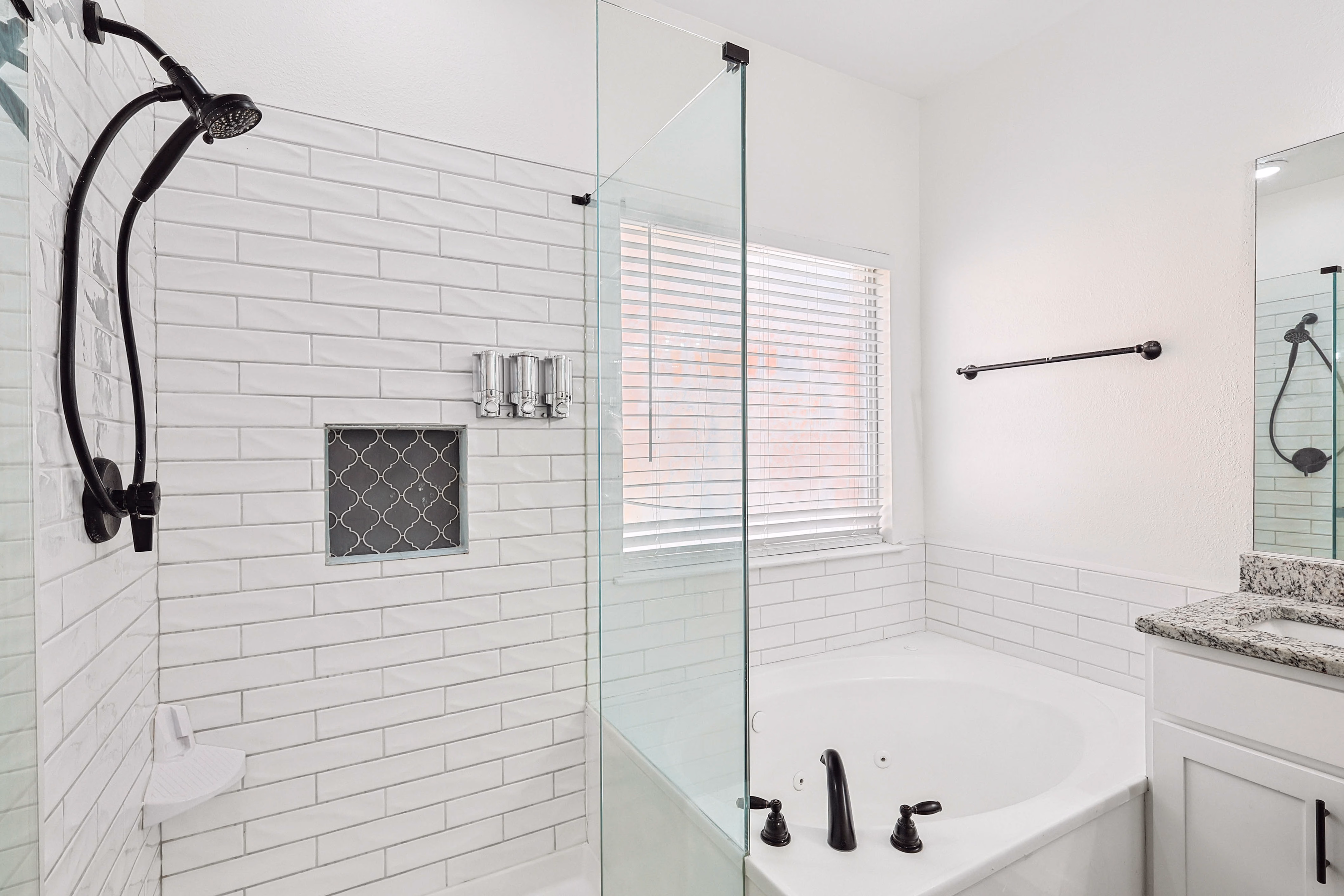 Primary bath — close-up of subway-tile shower with niche, corner soaking tub with bronze fixtures.