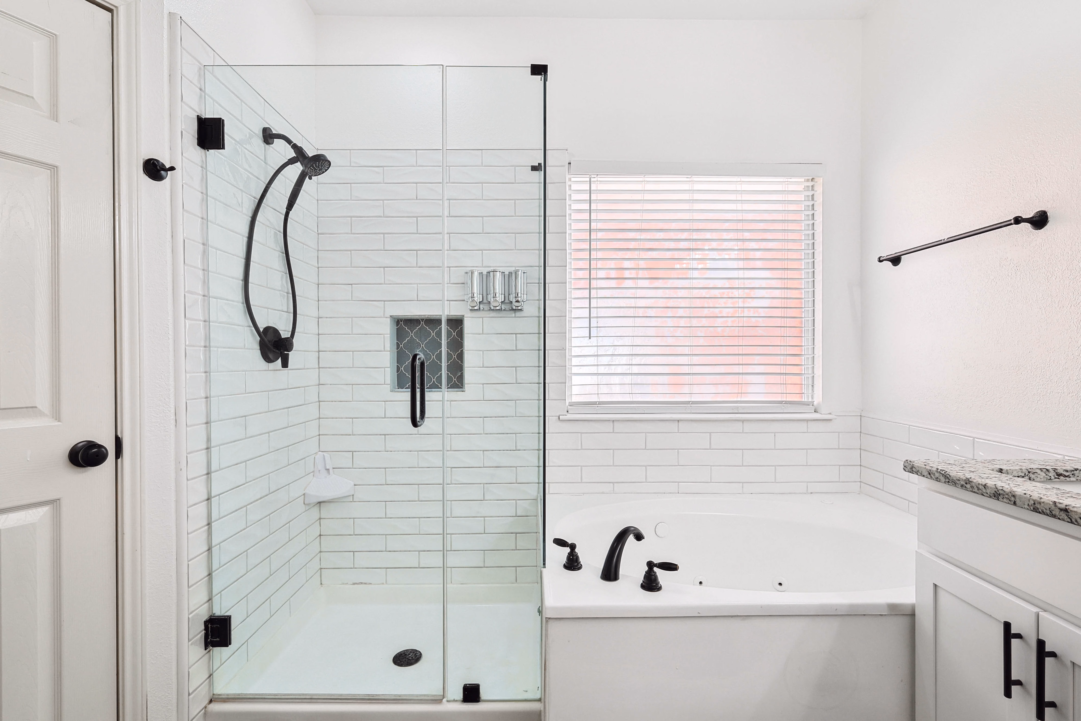 Primary bath — glass shower stall with handheld head, corner tub against subway-tile wainscot.