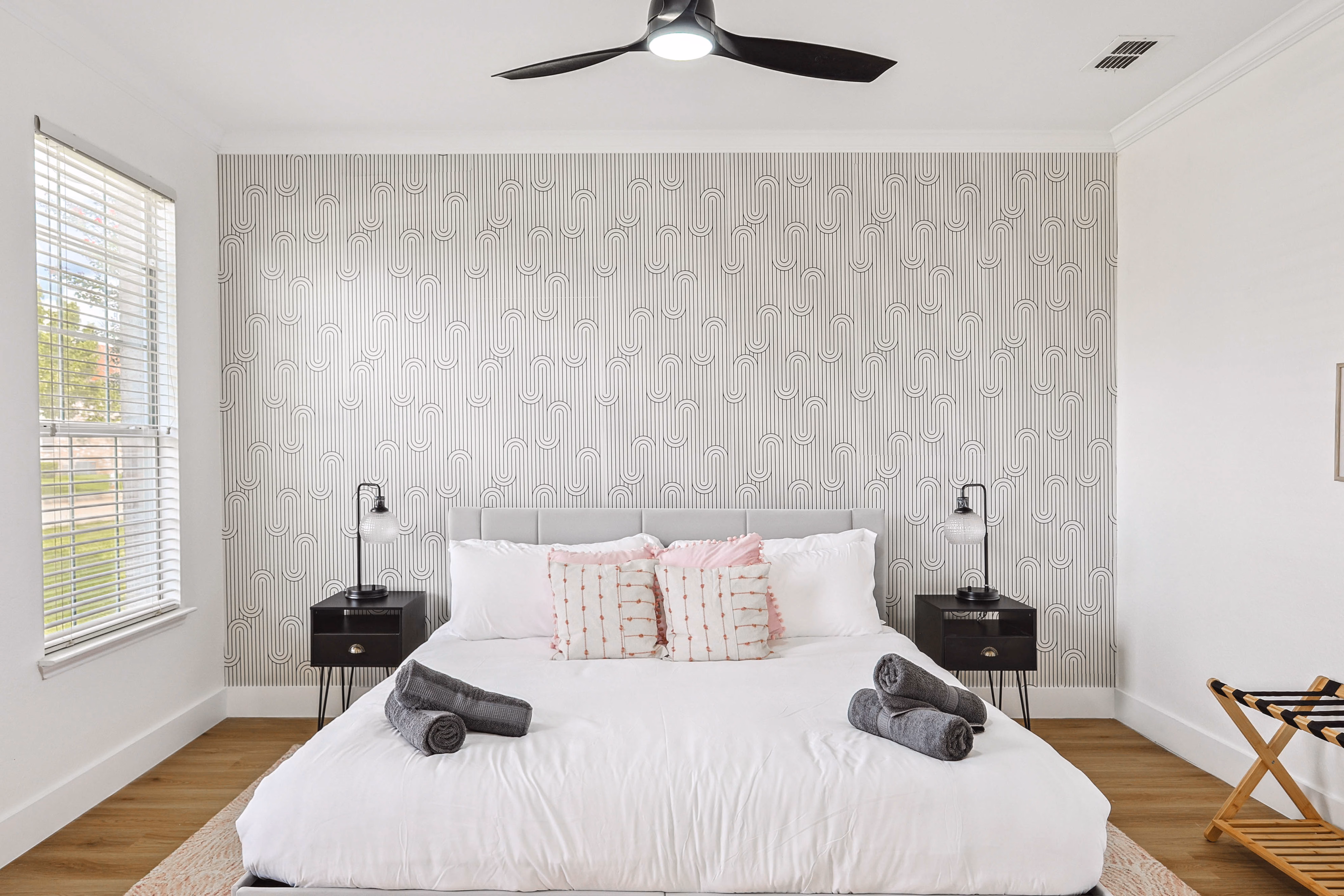 Downstairs guest bedroom — king bed against wave-pattern accent wall, ceiling fan, large windows.