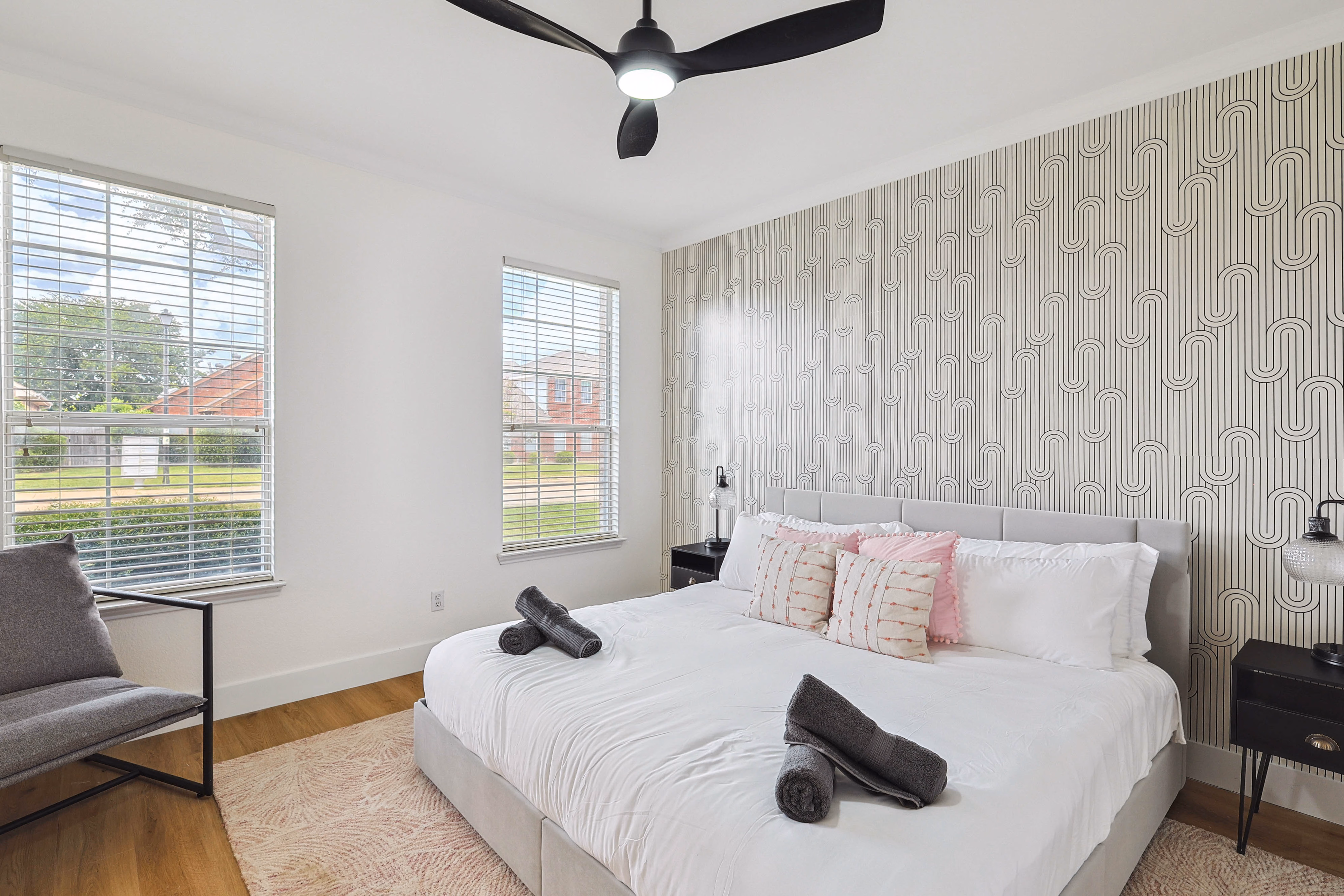 Downstairs guest bedroom — king bed with wave-pattern accent wall, large windows looking out to side yard.