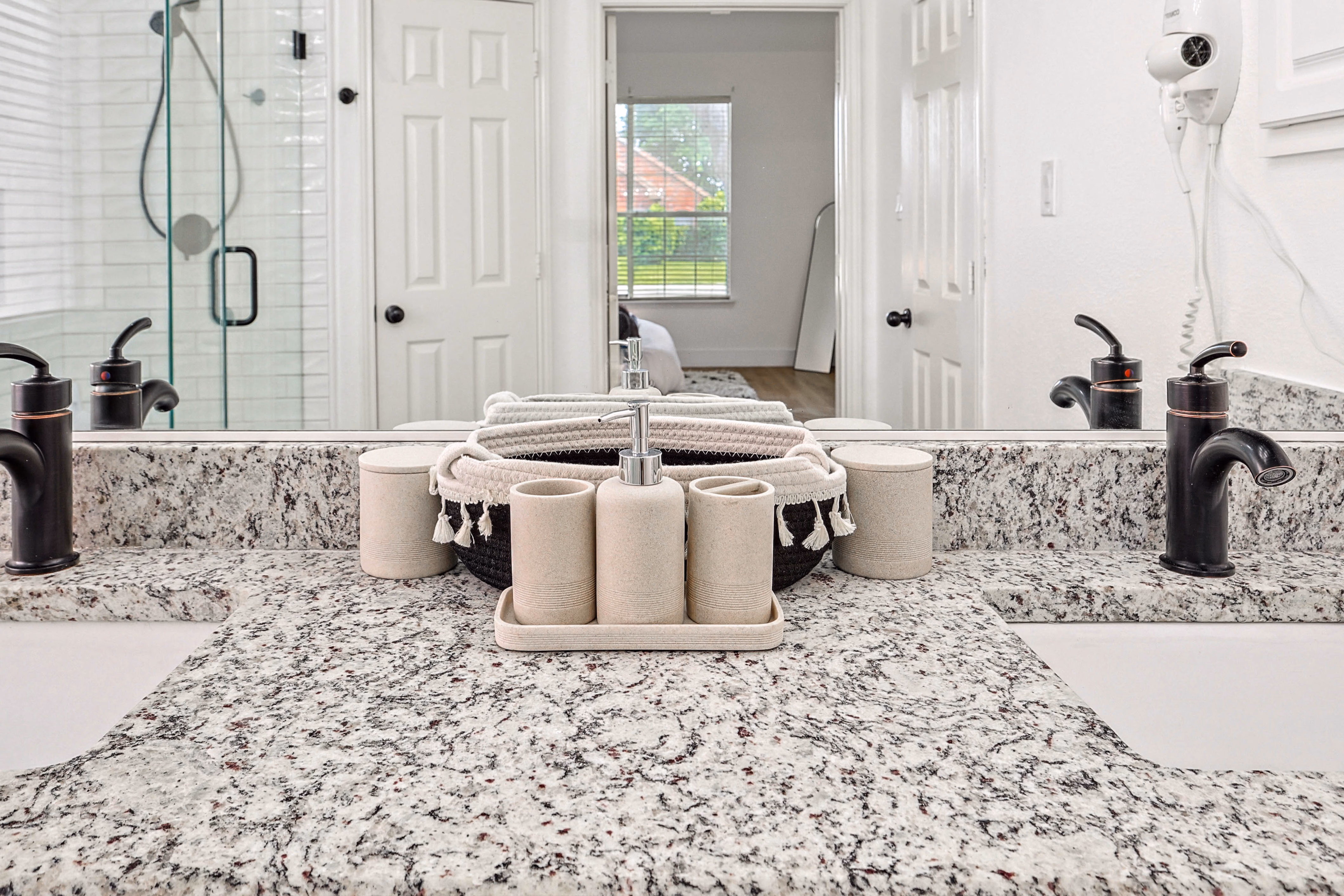 Primary bath — vanity countertop with toiletry tray, bronze faucets, shower visible in mirror.