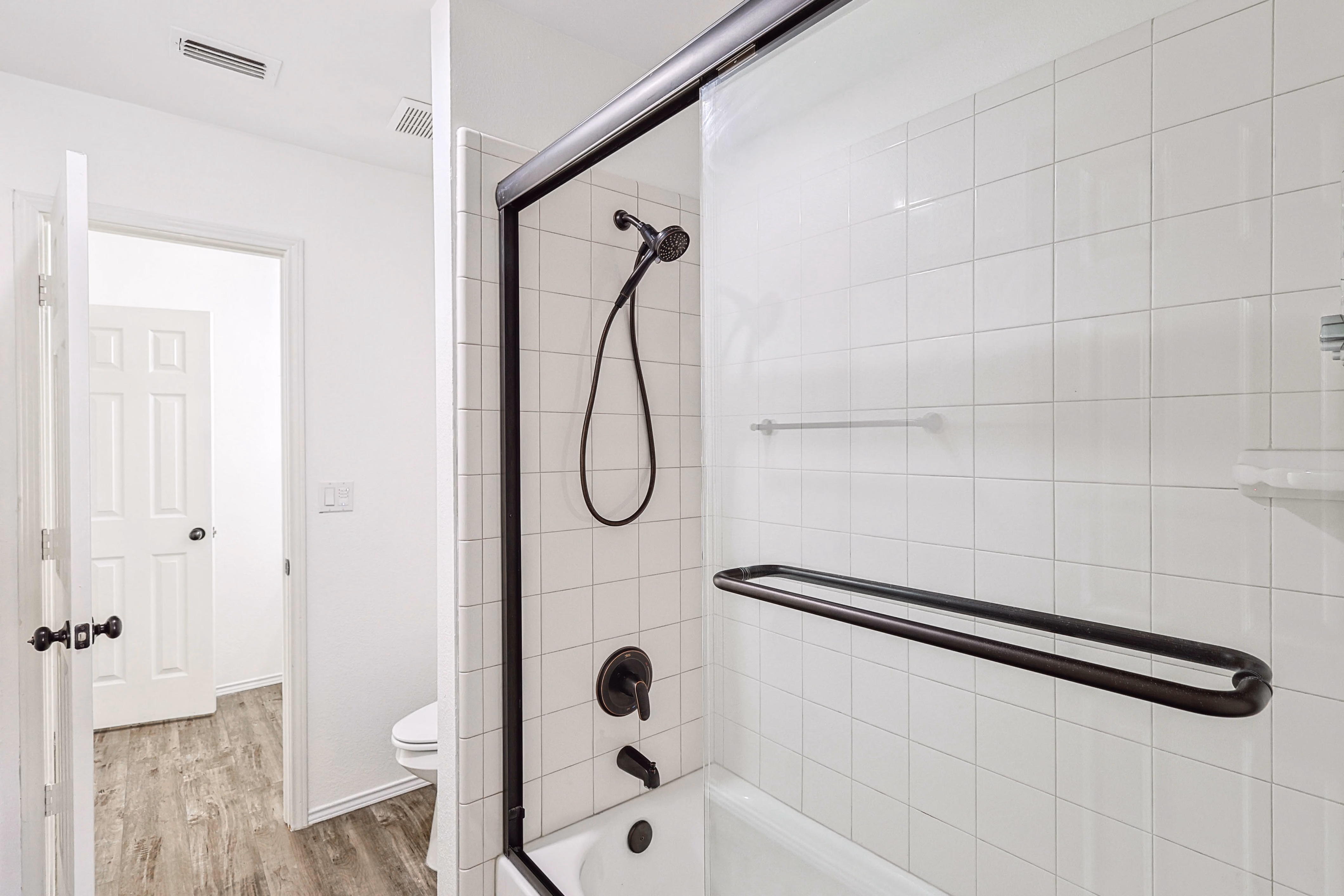 Upstairs hall bath — bypass tub/shower door with bronze grab bar, white tile surround.