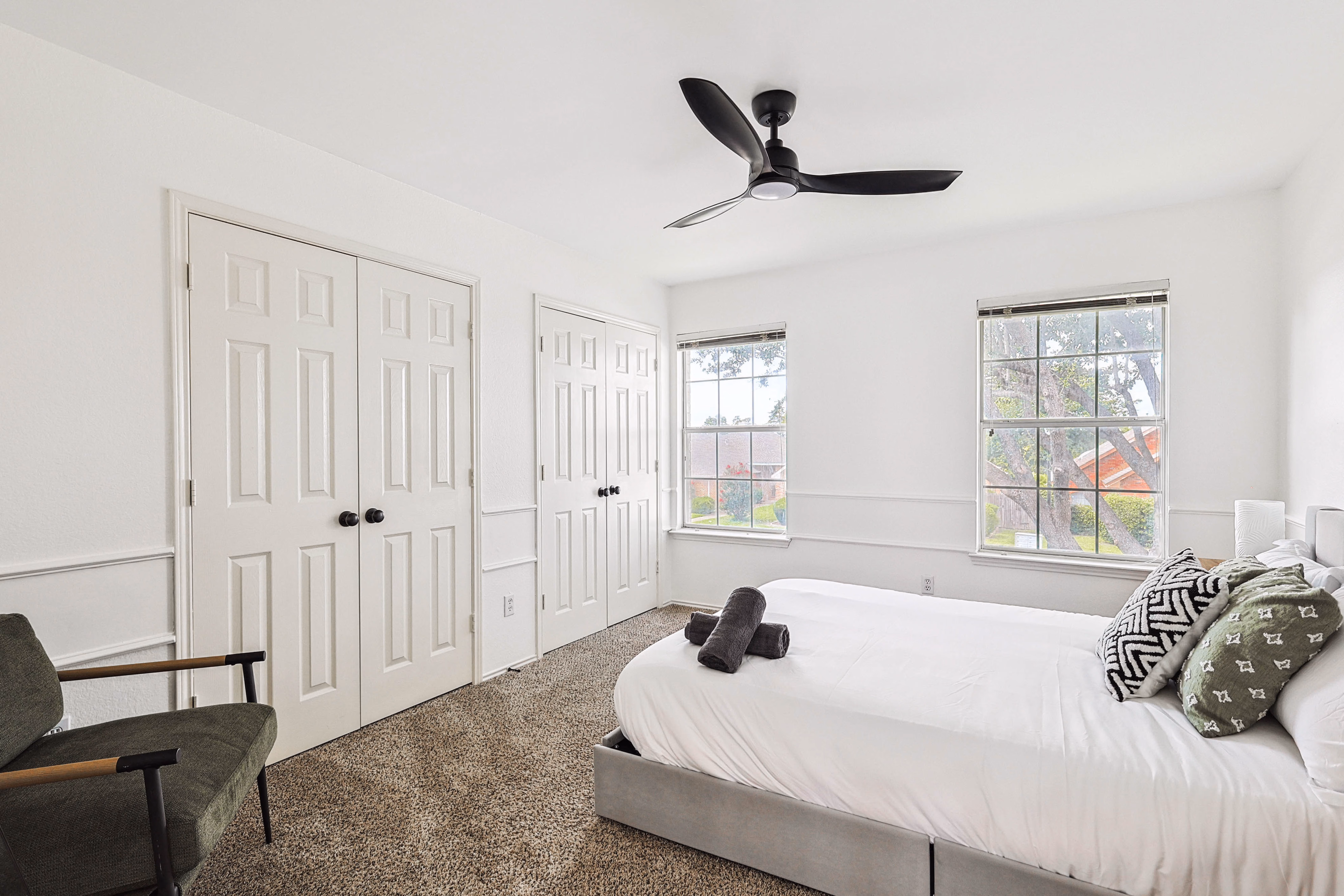 Upstairs back bedroom — queen bed, wainscot trim, two large windows over greenery.