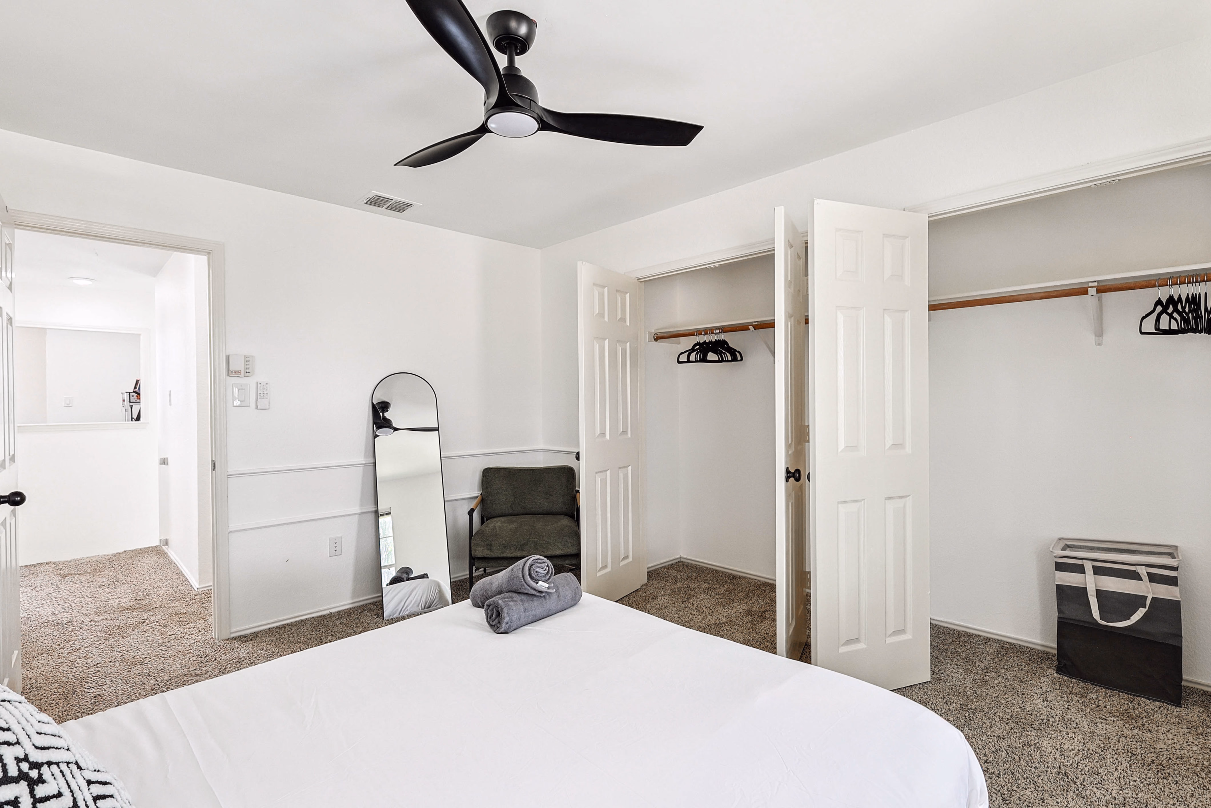 Upstairs back bedroom — leaning floor mirror, accent chair, open closet showing hangers and double bypass doors.