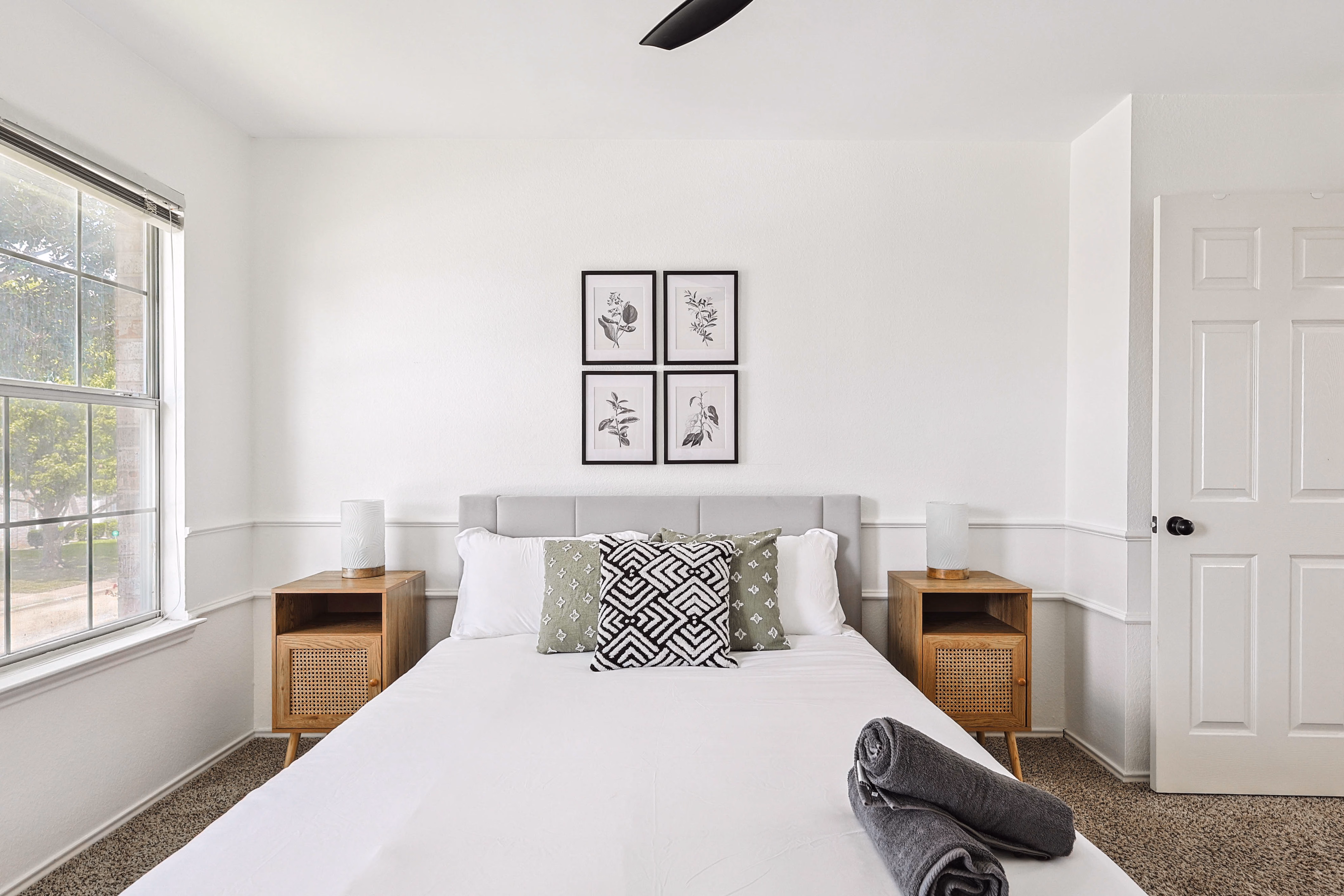 Upstairs bedroom — straight-on of queen bed with 4-frame botanical art and wainscot trim.