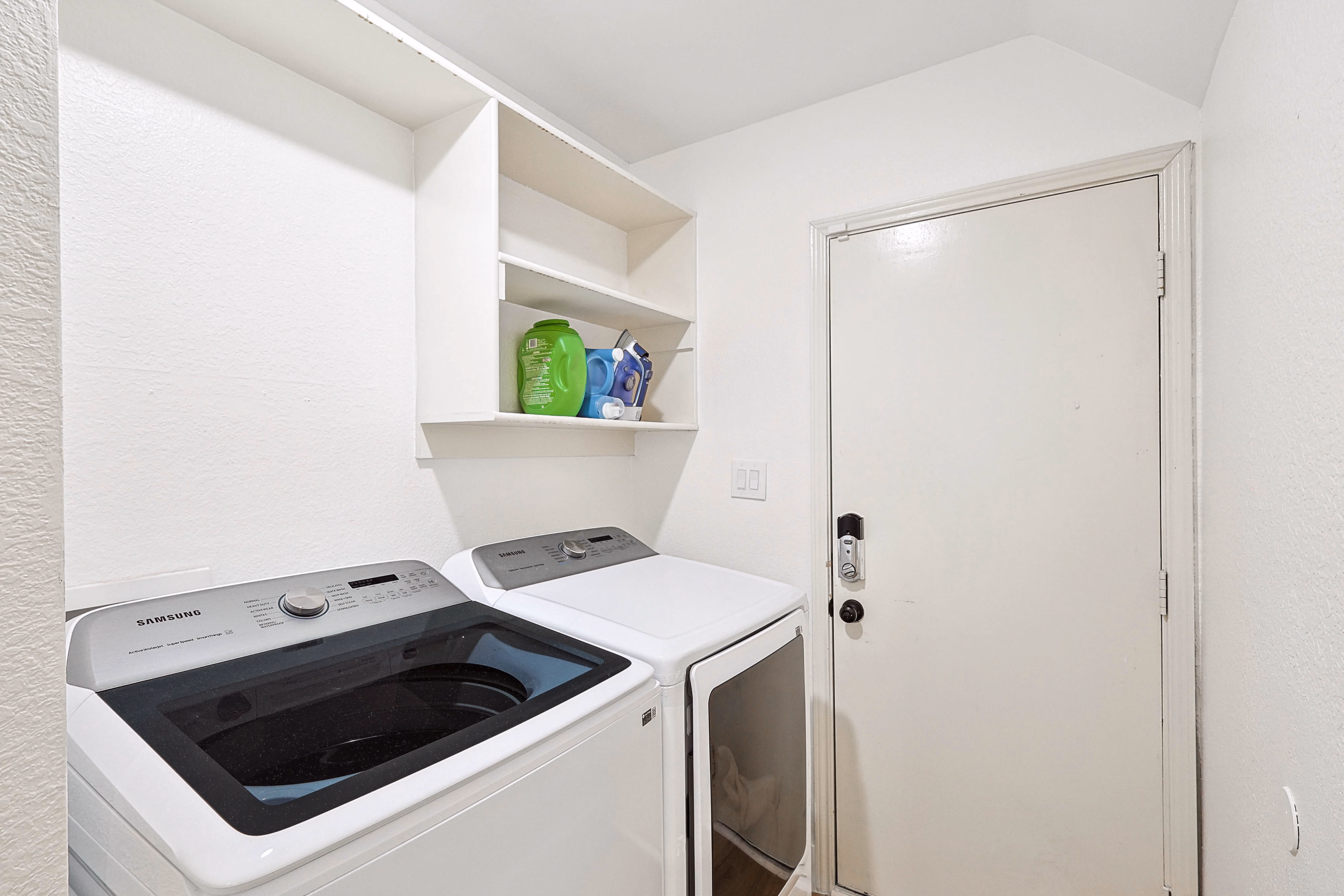 Laundry room — Samsung top-load washer and front-load dryer beside back exit door.
