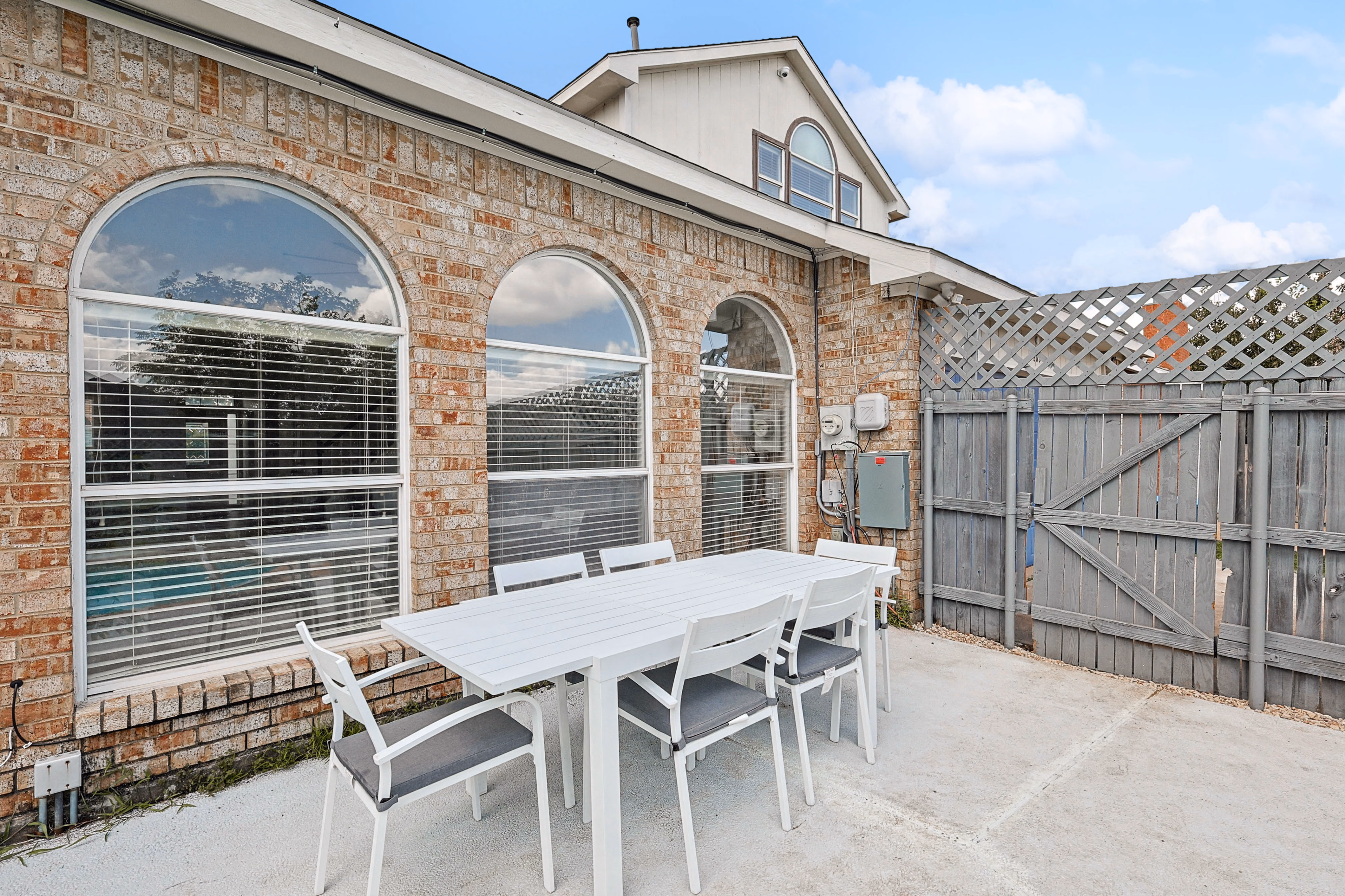 Back patio — outdoor dining table for six against brick wall with arched windows, side gate to driveway.
