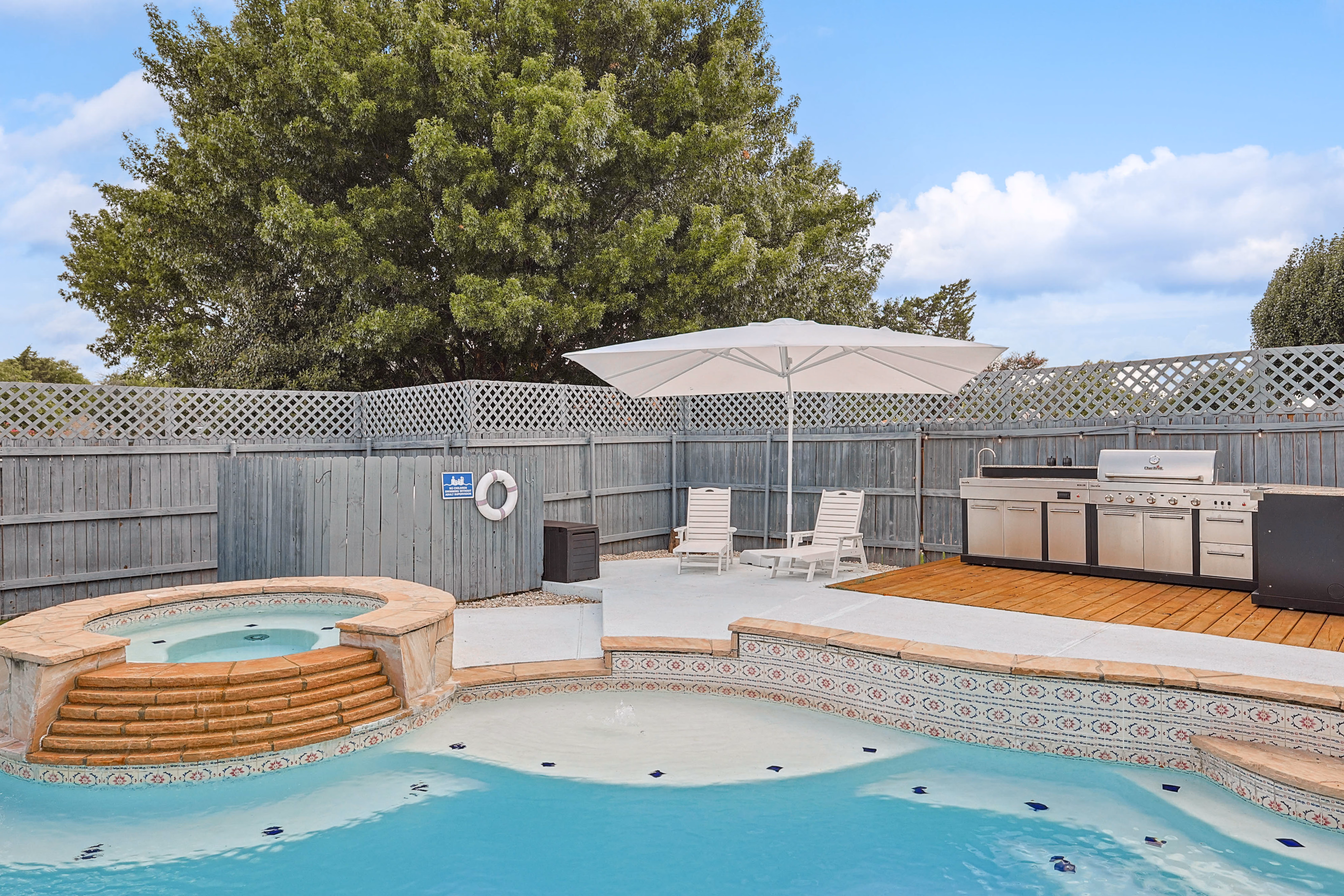 Hot tub spa attached to pool — Mediterranean tile mosaic spillover, umbrella shade beyond.