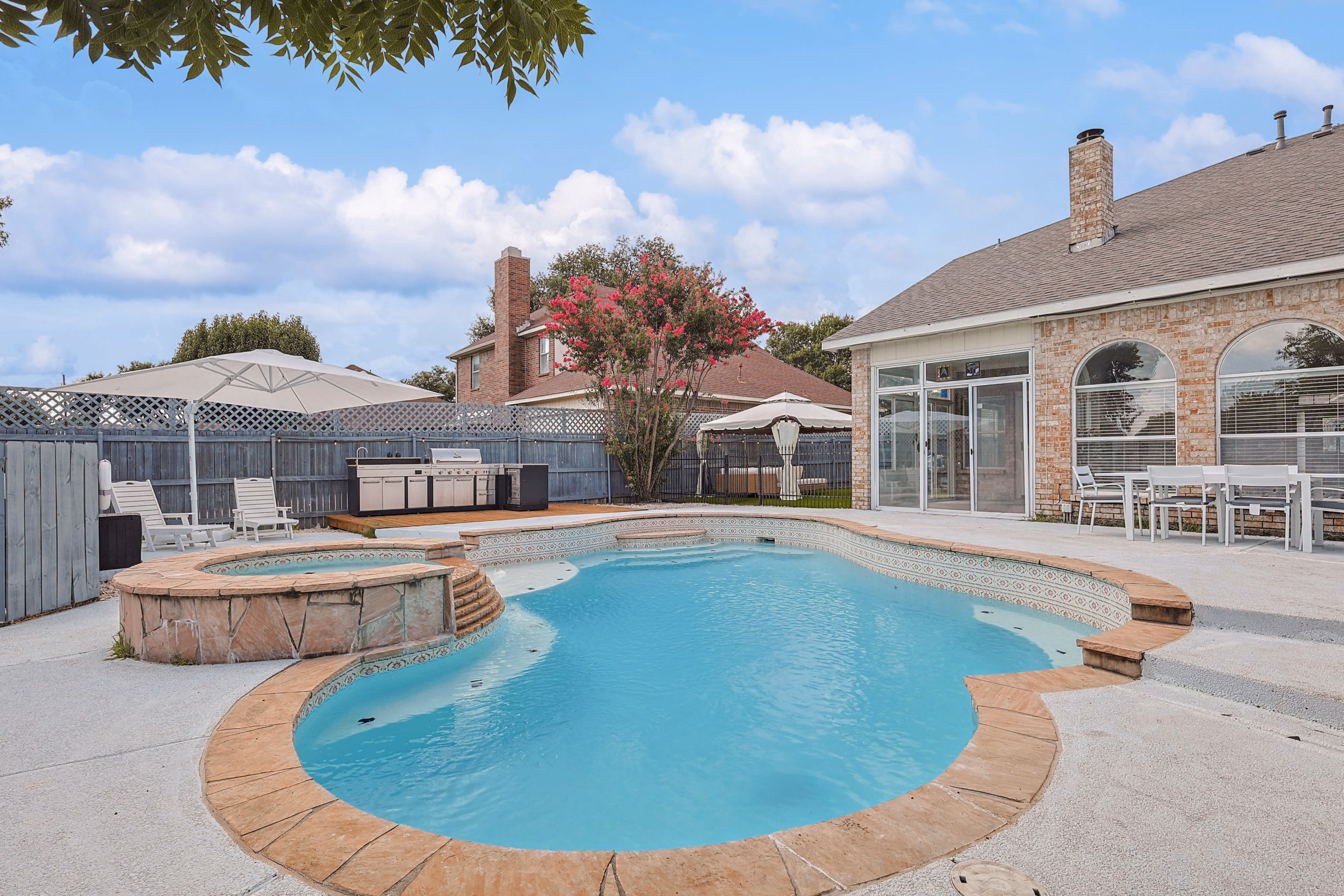Pool deck — wide view back toward the house showing brick facade, screened porch and outdoor kitchen.