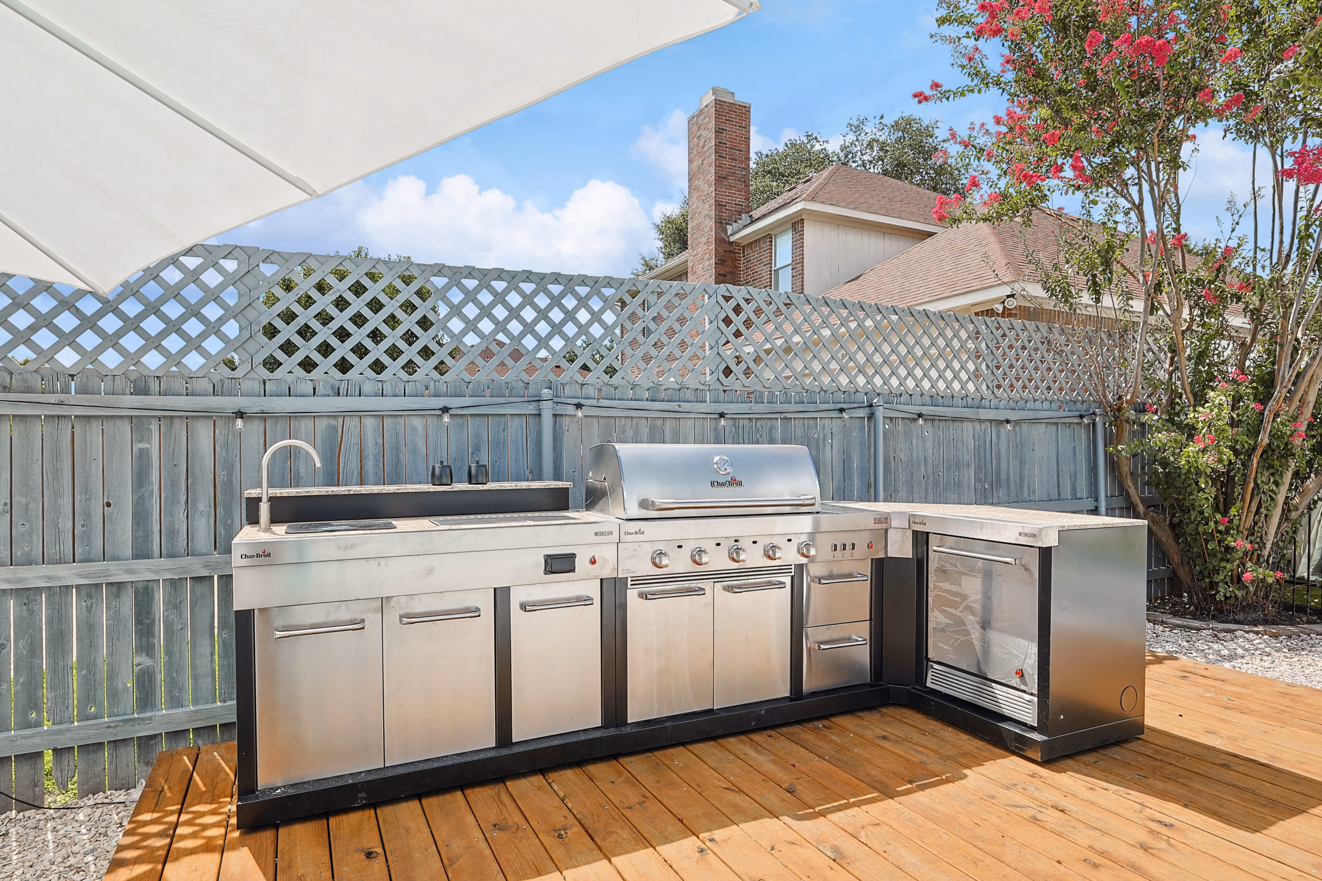 Outdoor kitchen — stainless 5-burner BBQ, side burner, sink and beverage fridge built into the wood deck.