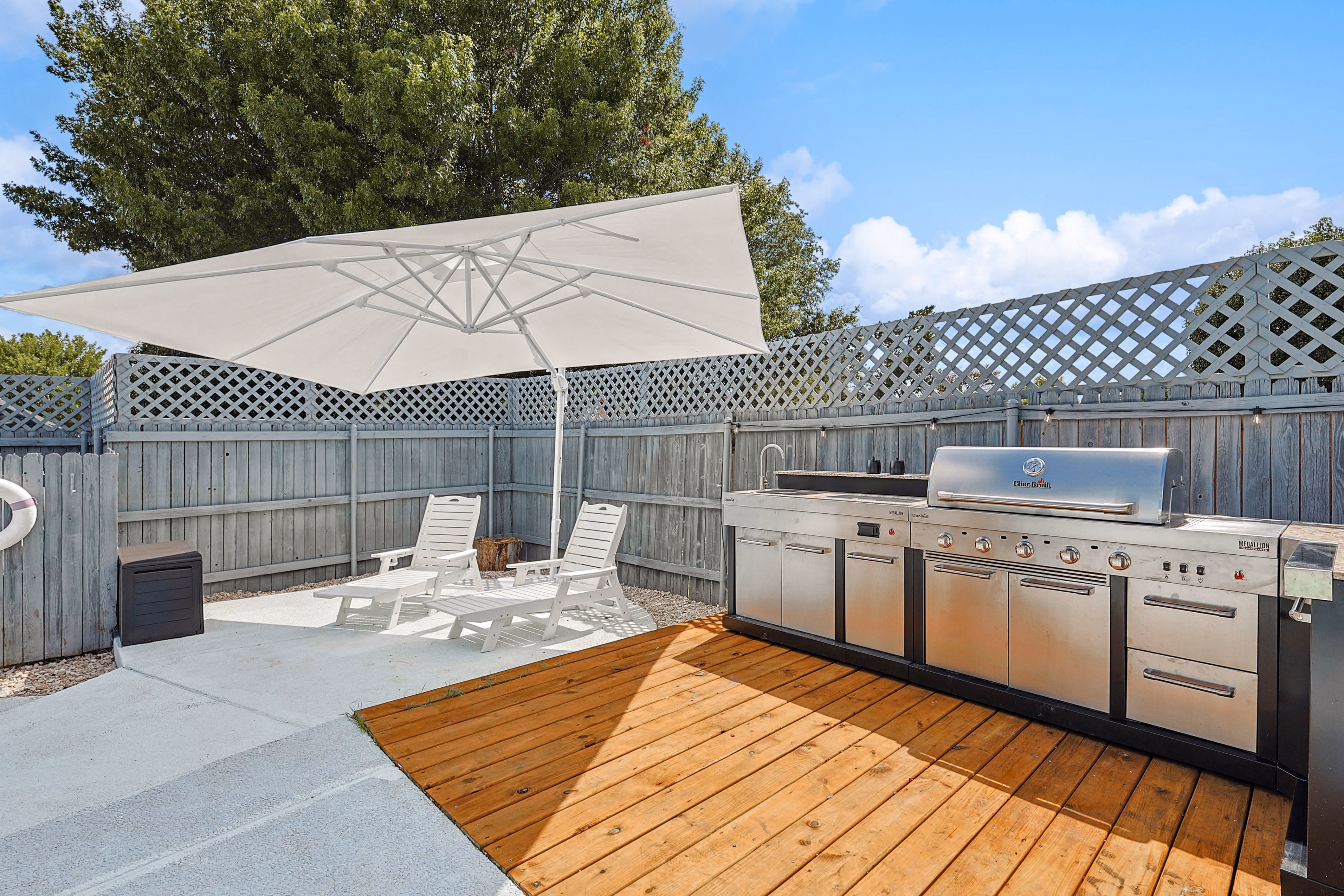 Outdoor kitchen — large patio umbrella, lounge chairs and BBQ station on wood deck against lattice fence.