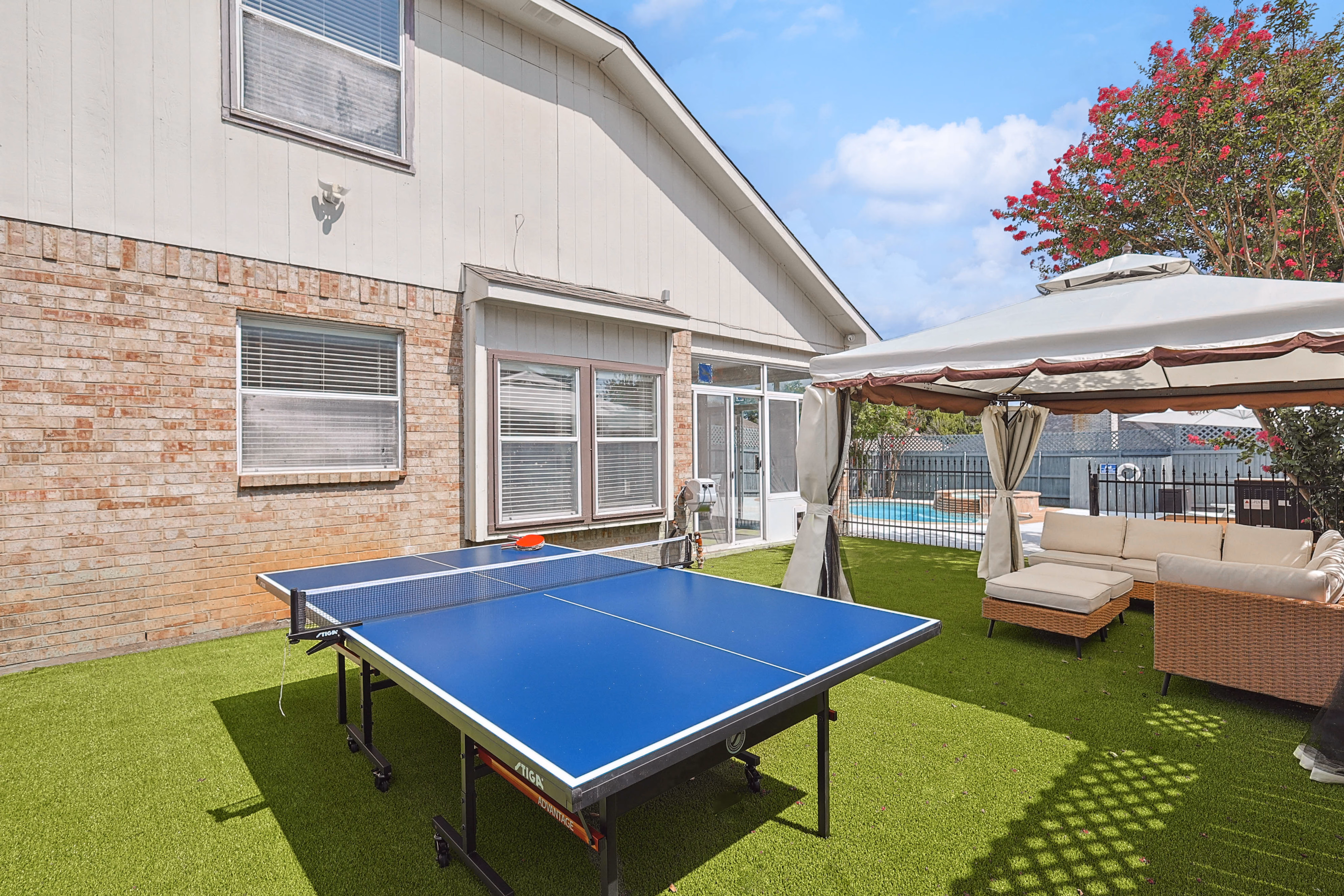 Side yard — ping pong table and canopy pavilion sectional against brick side of house.