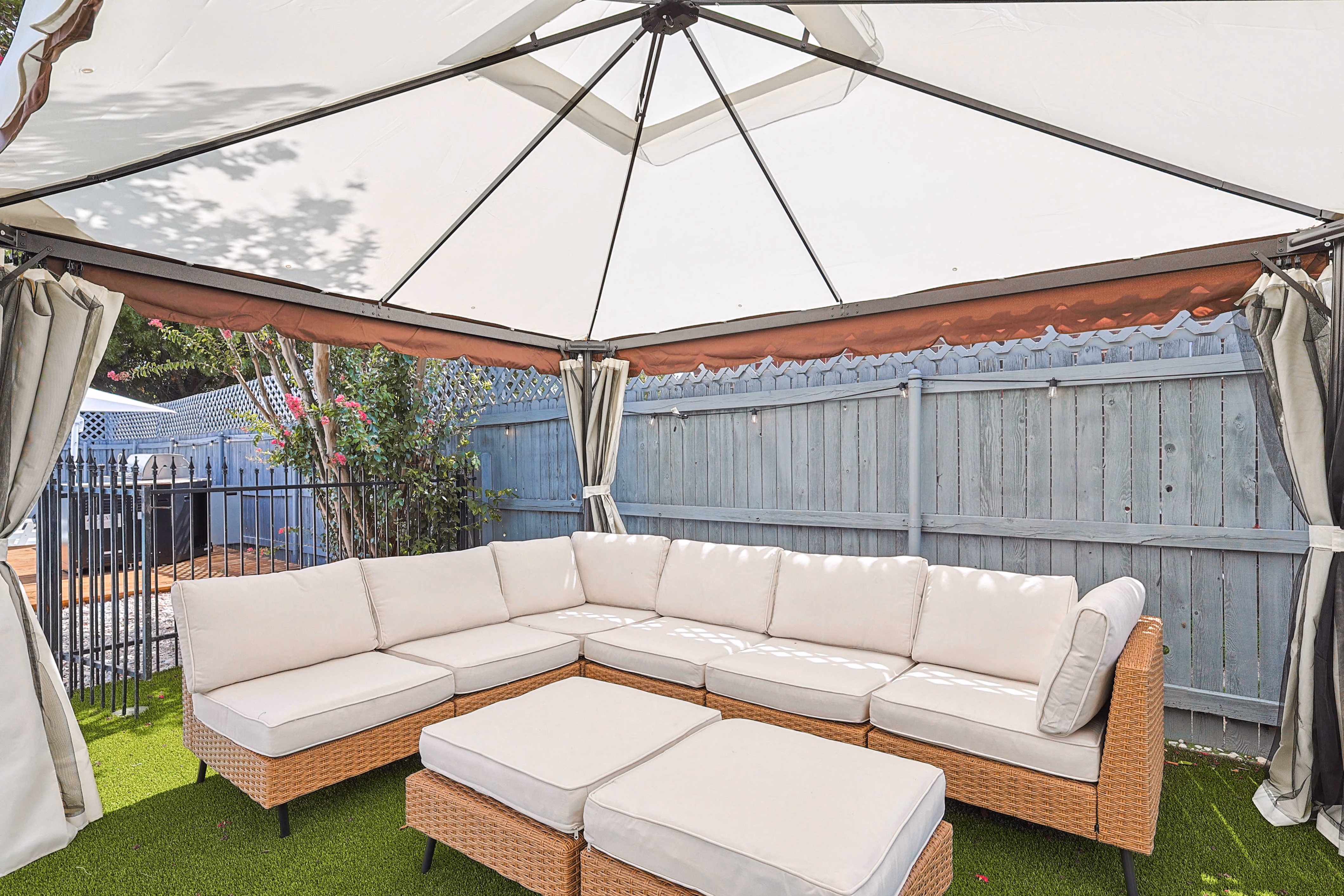 Canopy pavilion interior — rattan sectional with cushions under draped canopy curtains.