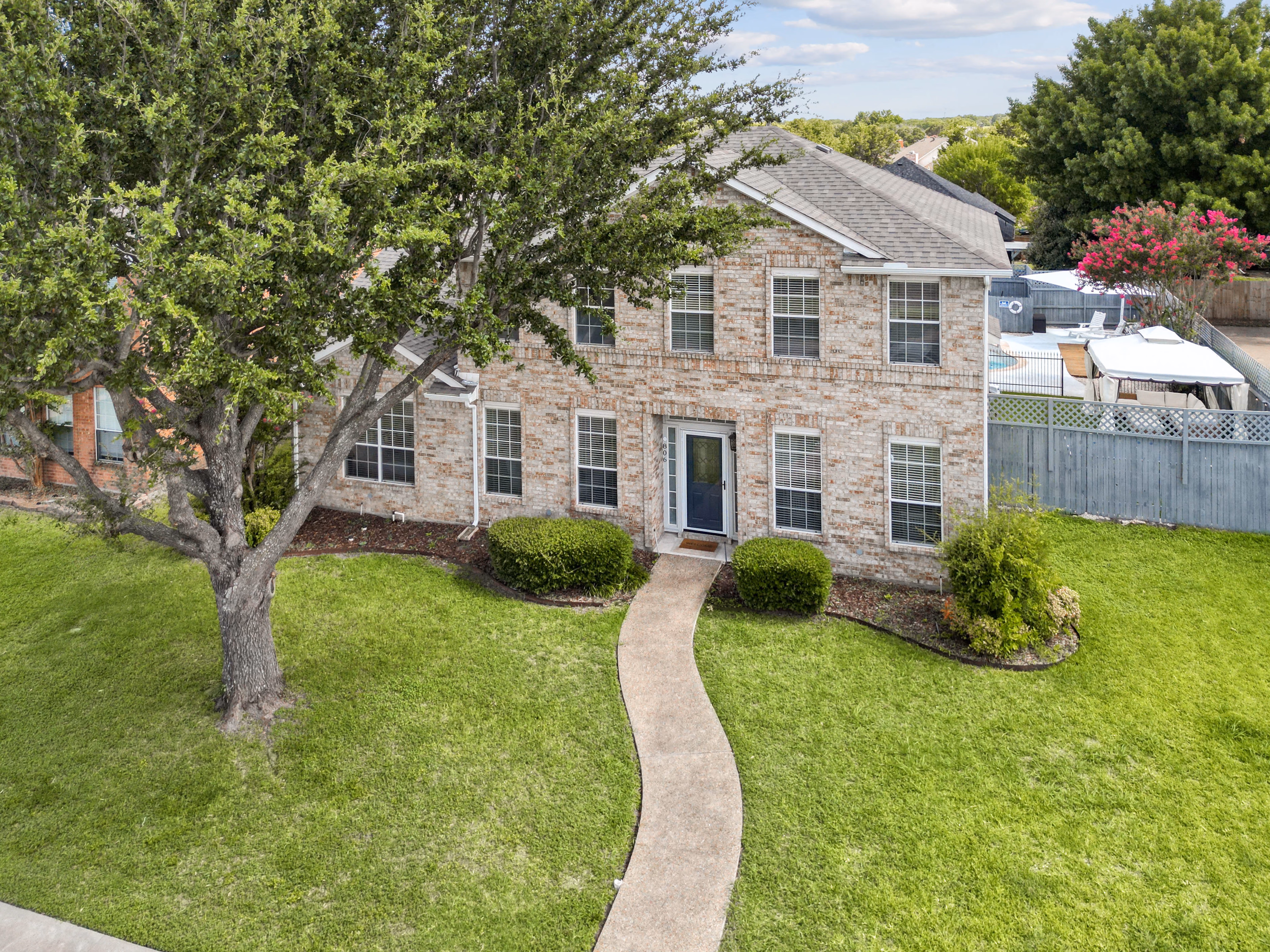 Aerial / drone — front of house from above, mature shade tree and curving walkway.