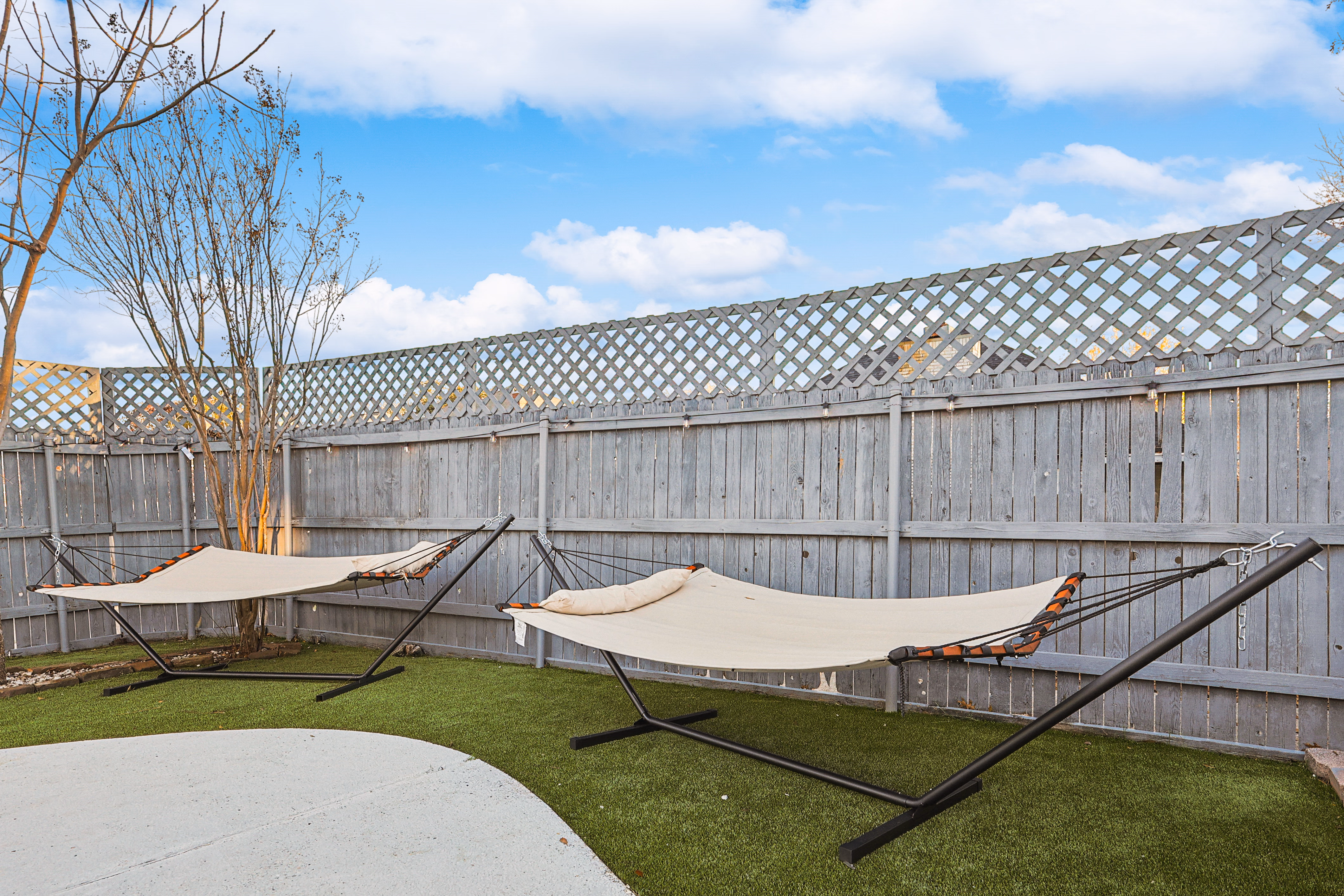 Side yard — pair of free-standing hammocks on astroturf against lattice-topped fence.