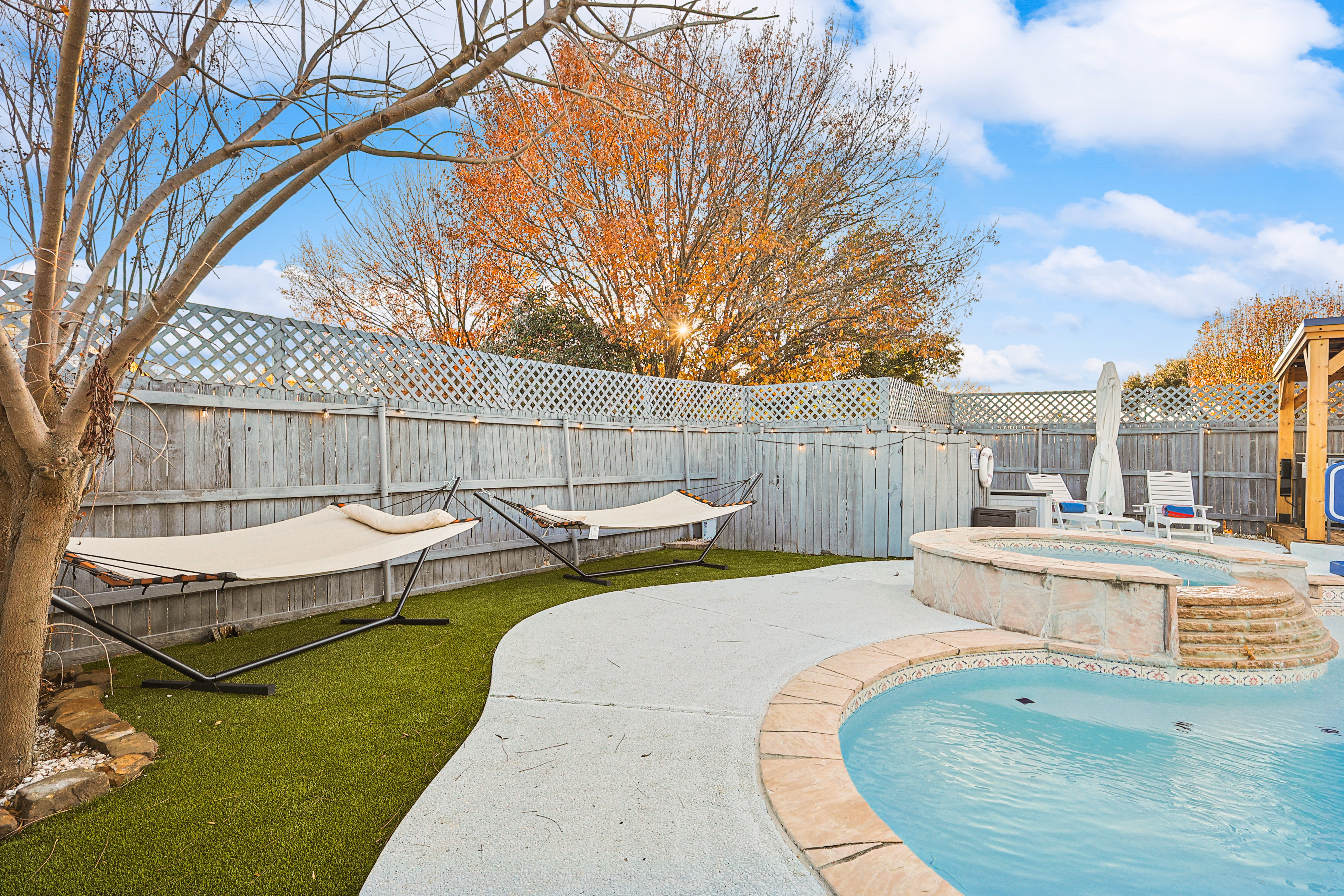 Side yard and pool — hammocks on astroturf, pool with hot tub beyond, wooden pavilion peek on right.
