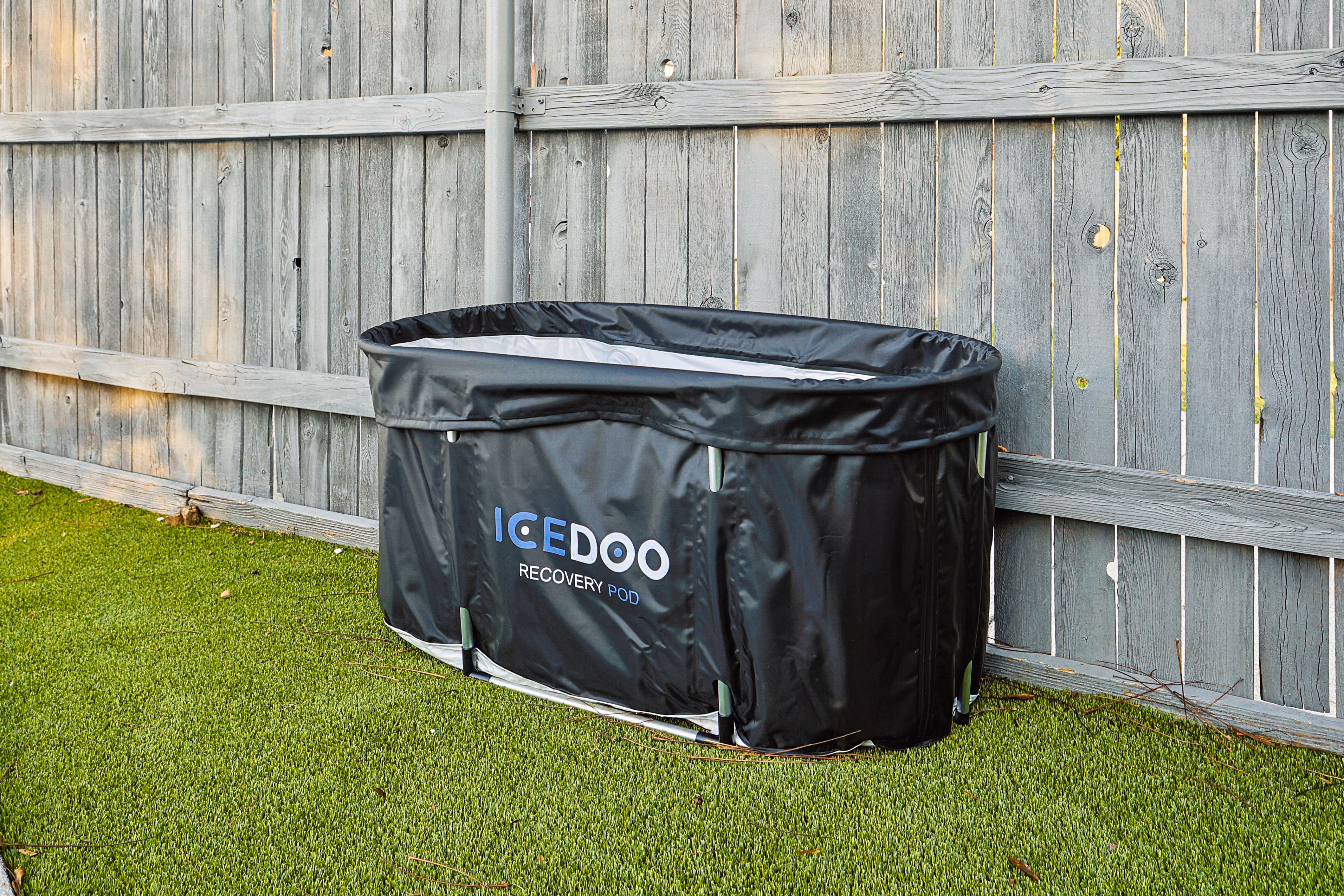 ICEDOO Recovery Pod ice bath on the side astroturf yard against the wood fence.