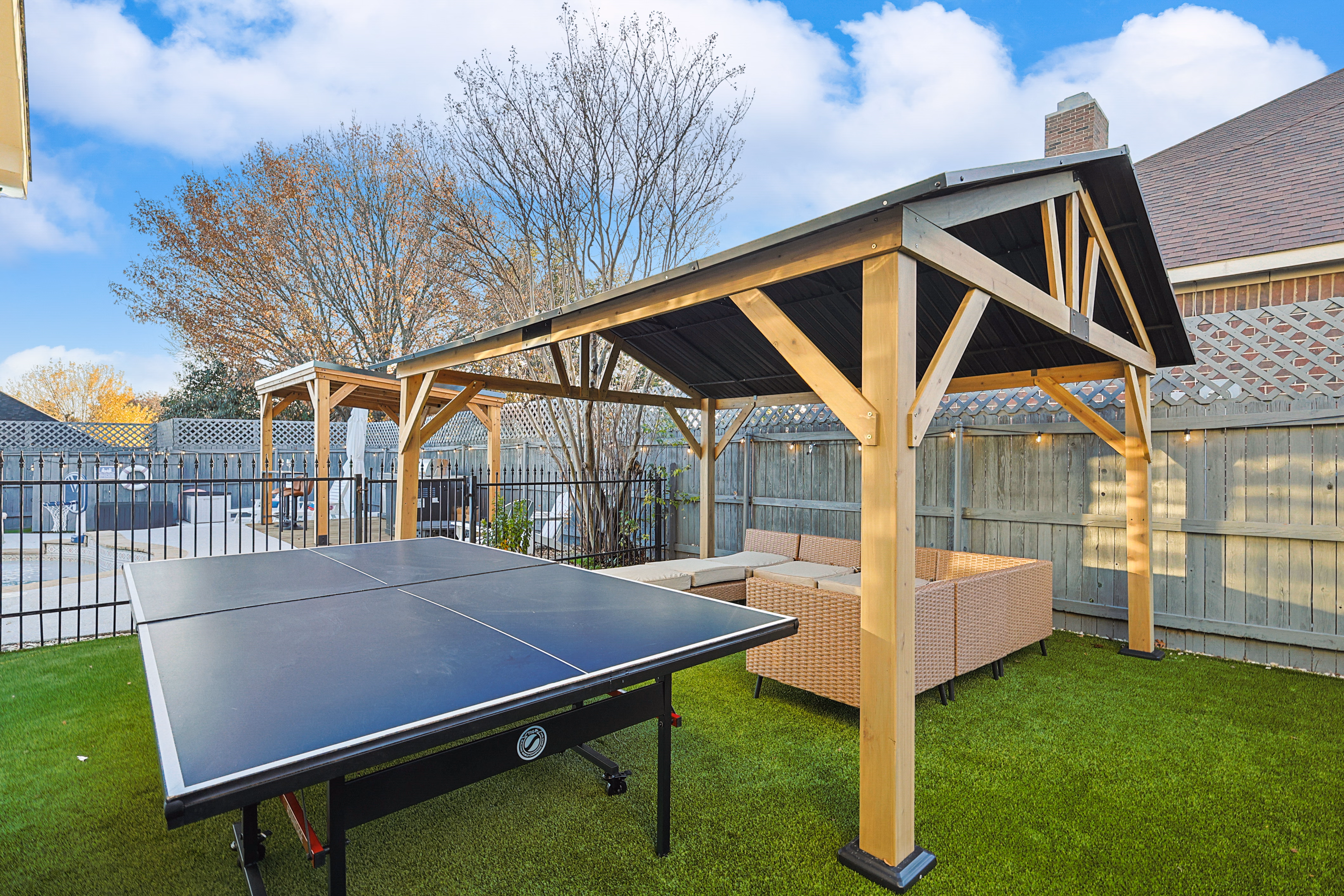 Wooden pavilion — sectional sofa and ping pong table from the back, looking toward the pool.